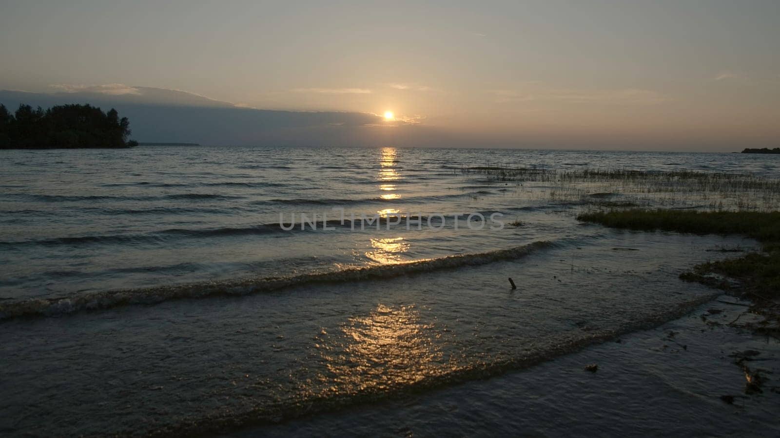 Grass and mud in shallow water with sunset. Creative. Grass in shallow water with water and small waves on horizon background. Waves and mud move with setting sun on summer evening.