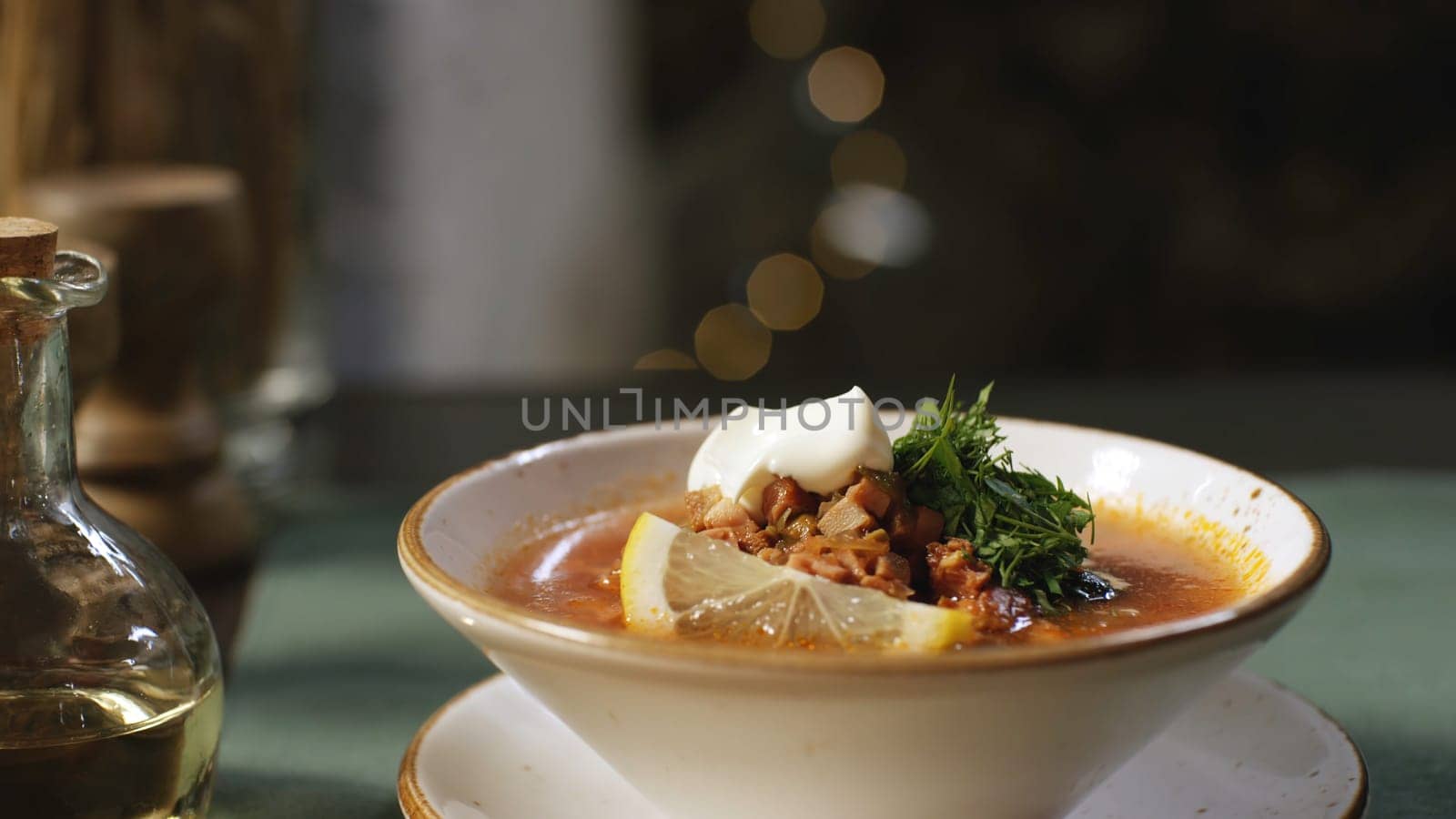 Close-up of hand putting the plate with Russian traditional soup solyanka on the table. Russian solyanka soup with meat, sausages and olives