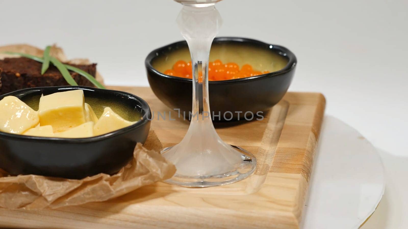 Diced butter, caviar, black bread. Bowl of red caviar with spoon served with sliced bread, butter and herbs on white background. Wholegrain bread, butter and red caviar, white background 4K