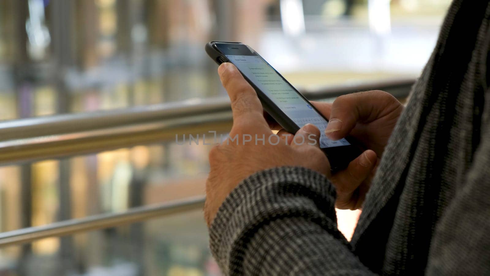 Close up of man hands texting a message on shopping mall background. Male hands using his smartphone for chatting in social net.