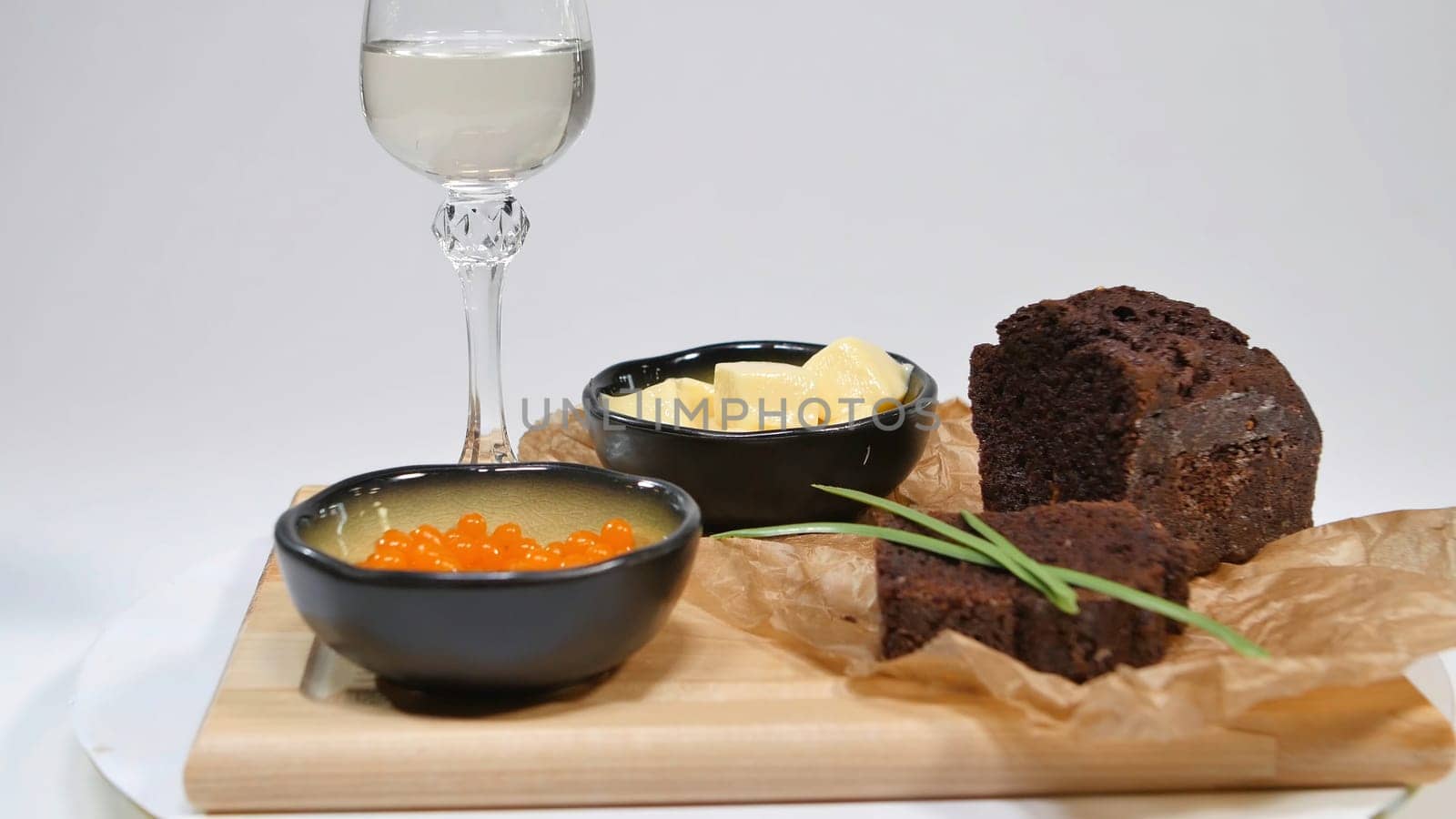 Fresh red caviar with basil and butter on bread in studio. Bred with red caviar with wine glasses on background. Cold Russian vodka with ice and small snacks sandwiches with butter and red salmon caviar on an old wooden table in rustic style, selective focus