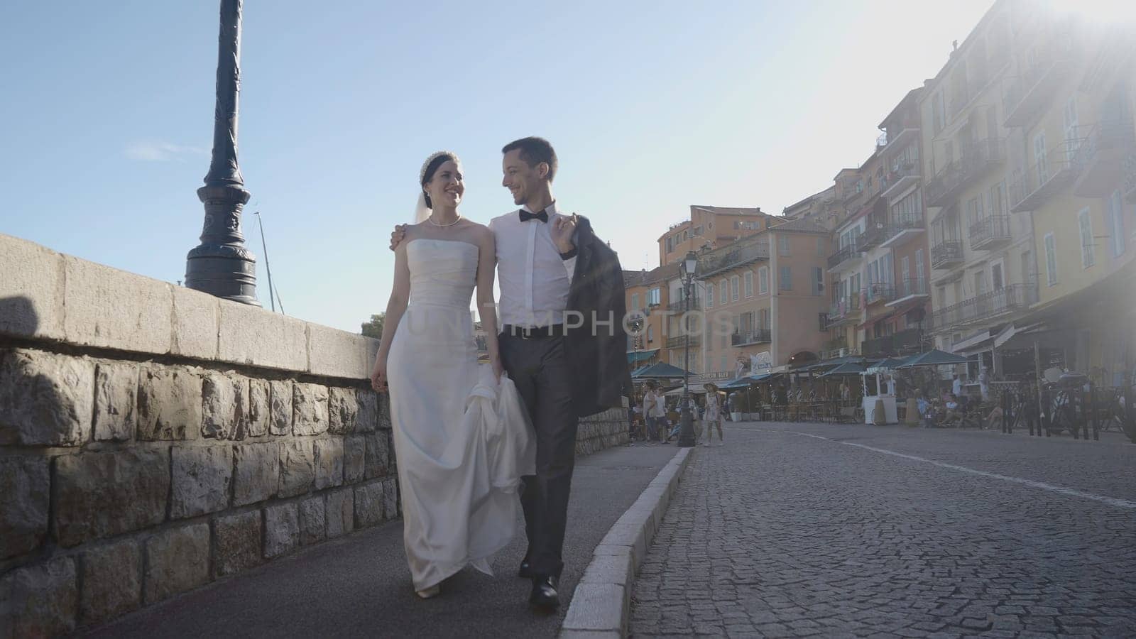 Beautiful newlyweds walking in ancient city. Action. Couple of newlyweds in outfits are walking along old street of city. Happy newlyweds walk around city on sunny day.