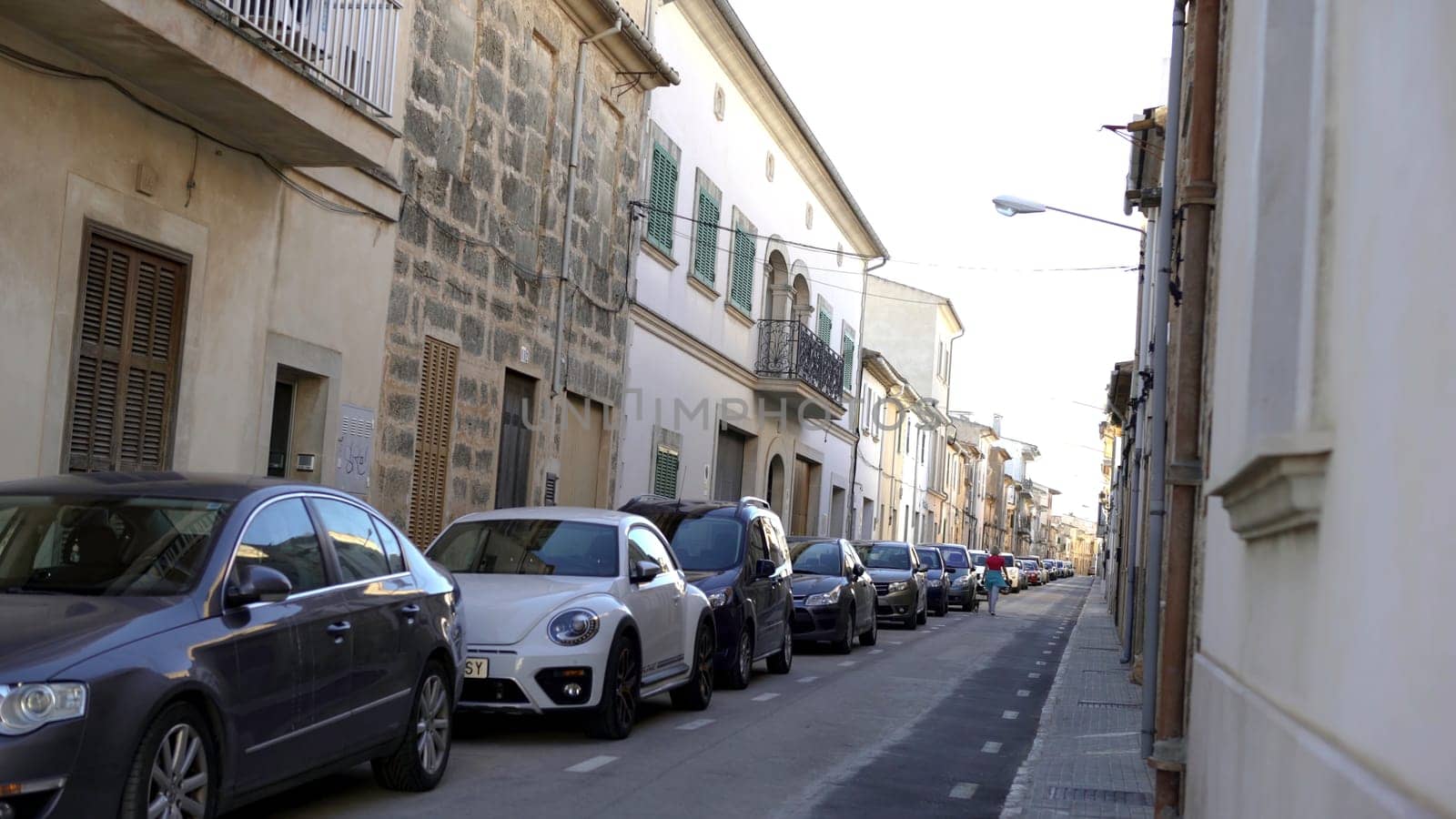 View of narrow streets of european city in summer. Art. Woman walks with dog on narrow street with parked row of cars on summer vacation.