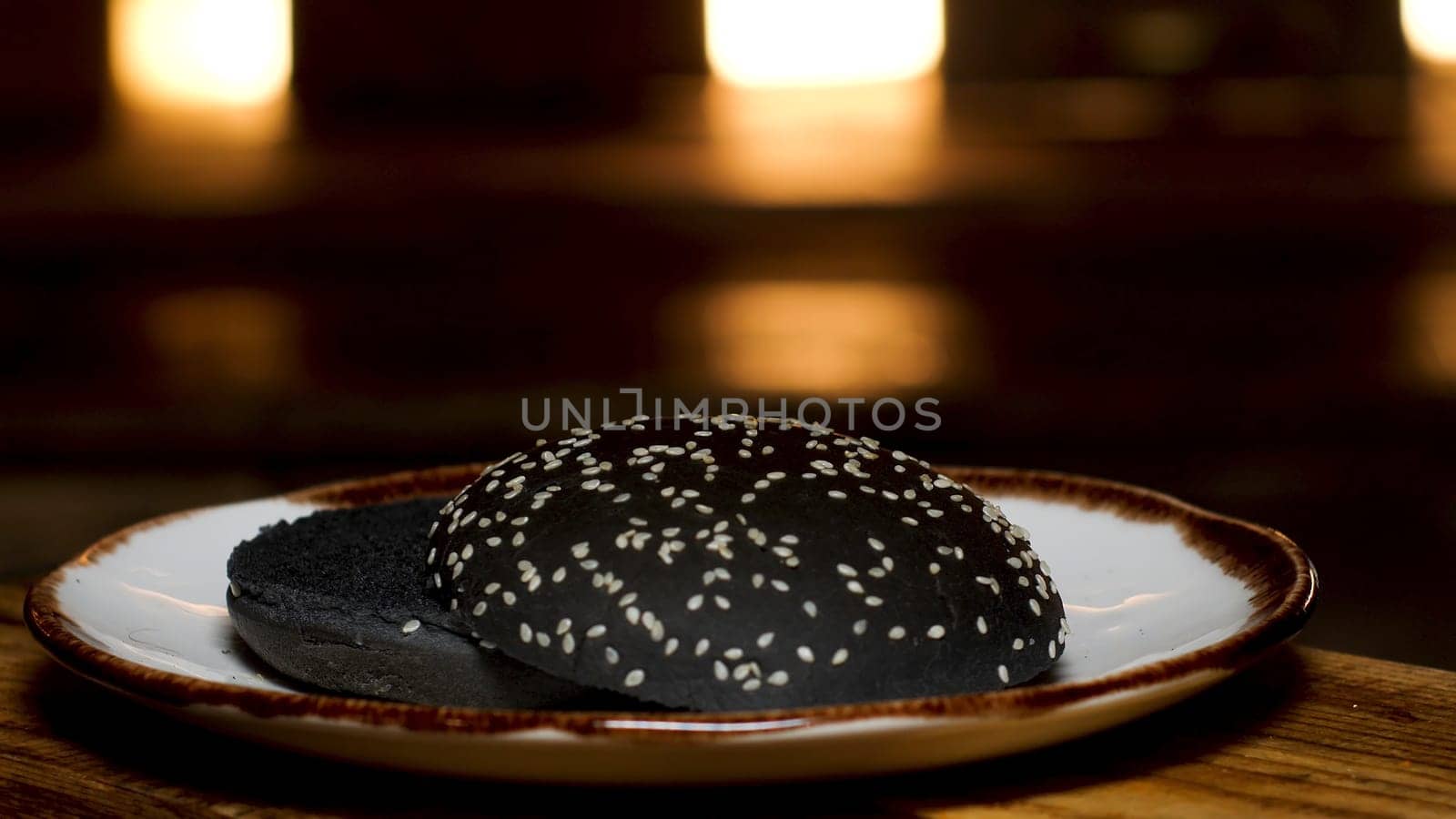 Close up of black bread with sesame seeds lying on a plate on the wooden table. Homemade bread for hamburgers preparation.