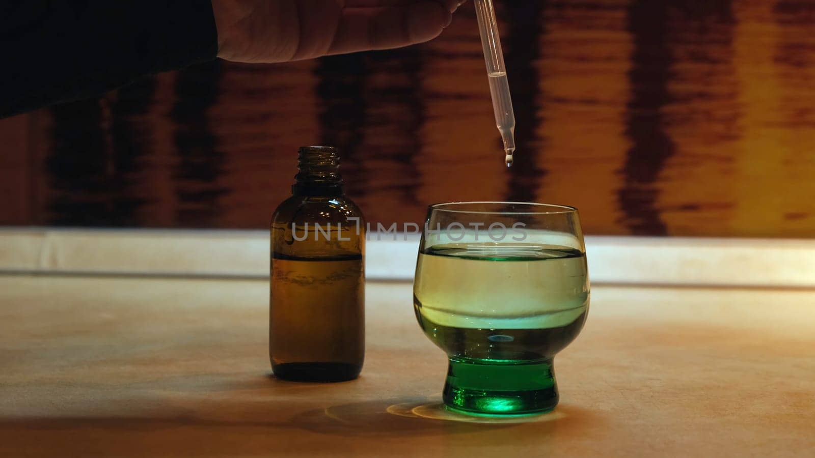 Close up of woman hand pouring drops into a glass of water. Female dripping antiviral drops into the green glass of water, medicine and covid 19 illness theme.