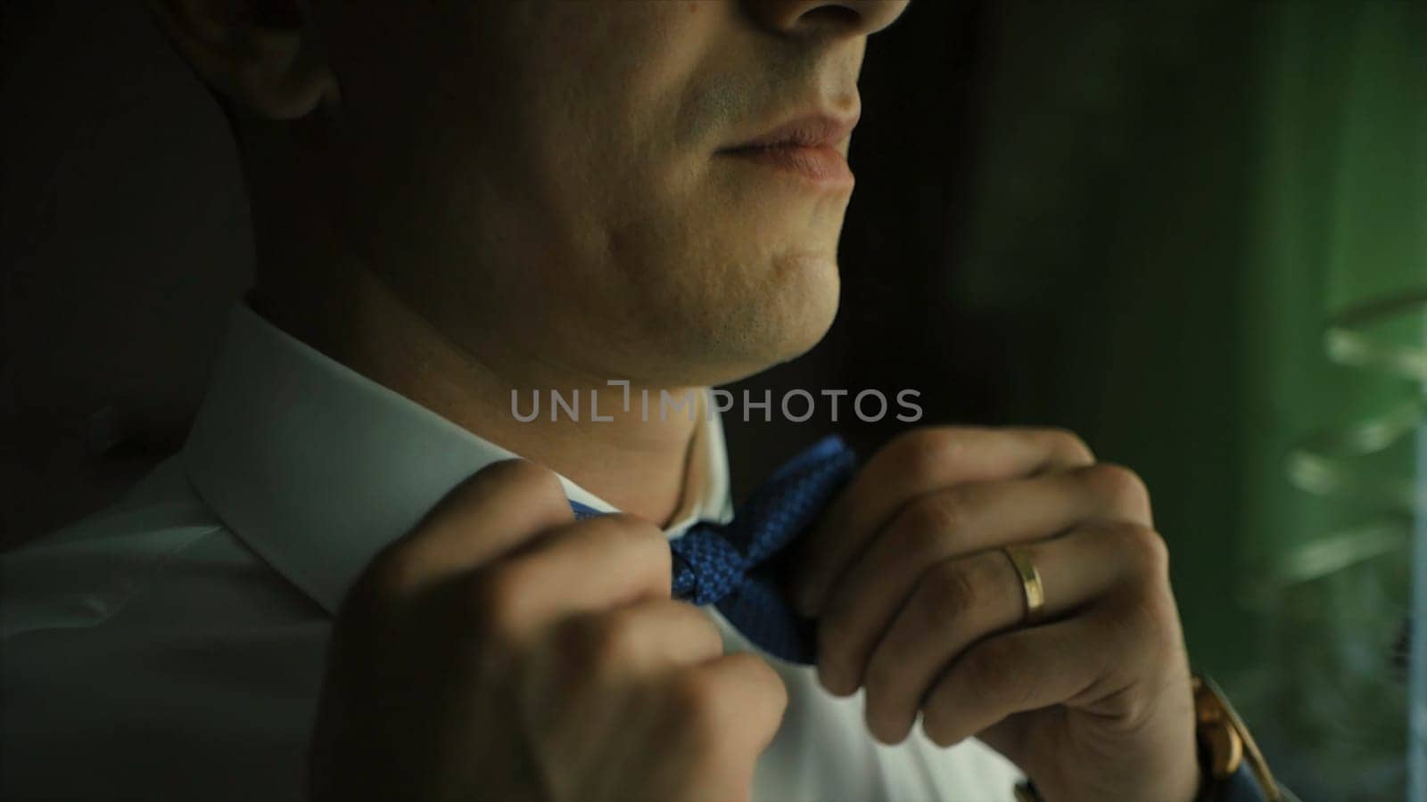 Man adjusting bow tie. Clip. Close-up of young man in white shirt adjusting his bowtie while standing.
