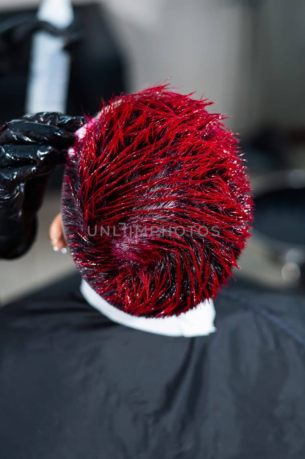 The hairdresser removes excess dye from the skin of a female with a cotton pad.Asian woman with a short haircut in a hairdressing salon