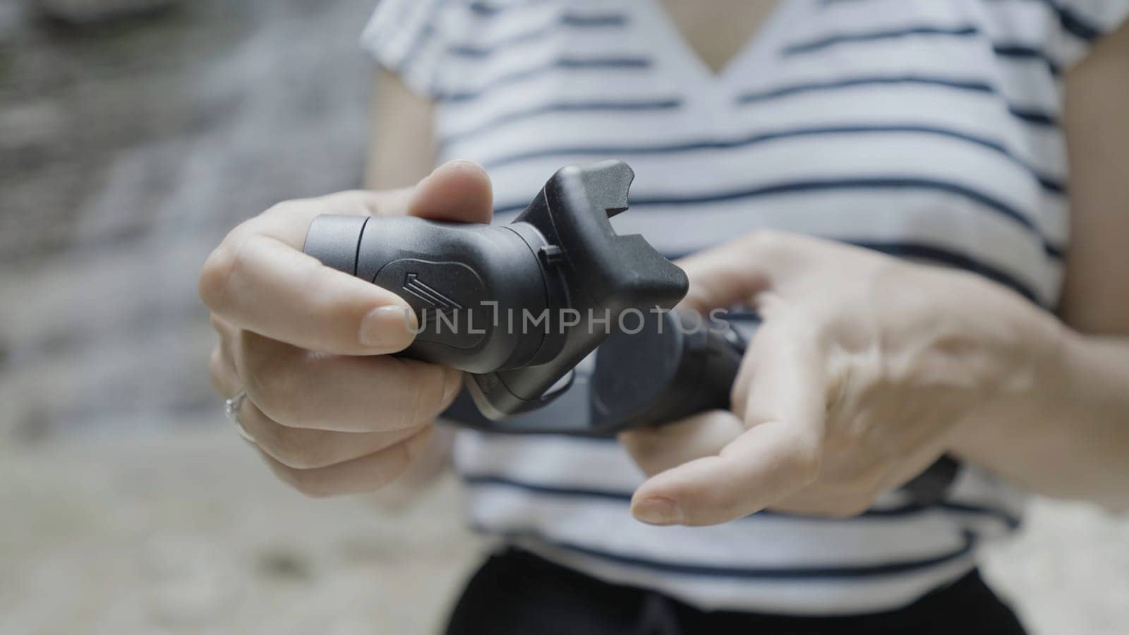 Close up of female hands holding smartphone tripod on blurred natural background. Action. Woman unfolding tripod