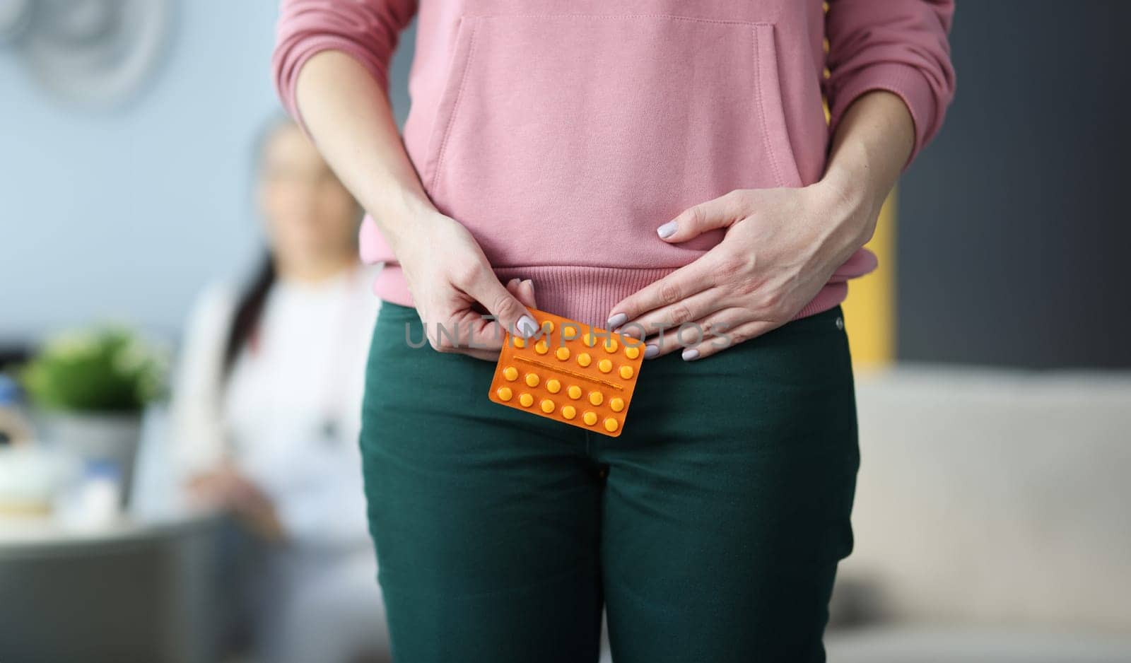Woman holding blister with pills in lower abdomen in clinic closeup. Gynecological problems concept