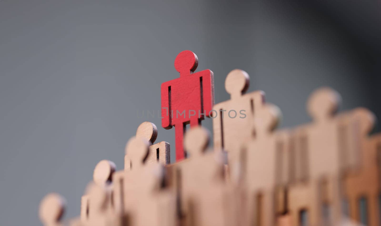 Red wooden figurine standing above others closeup. Leadership skills concept