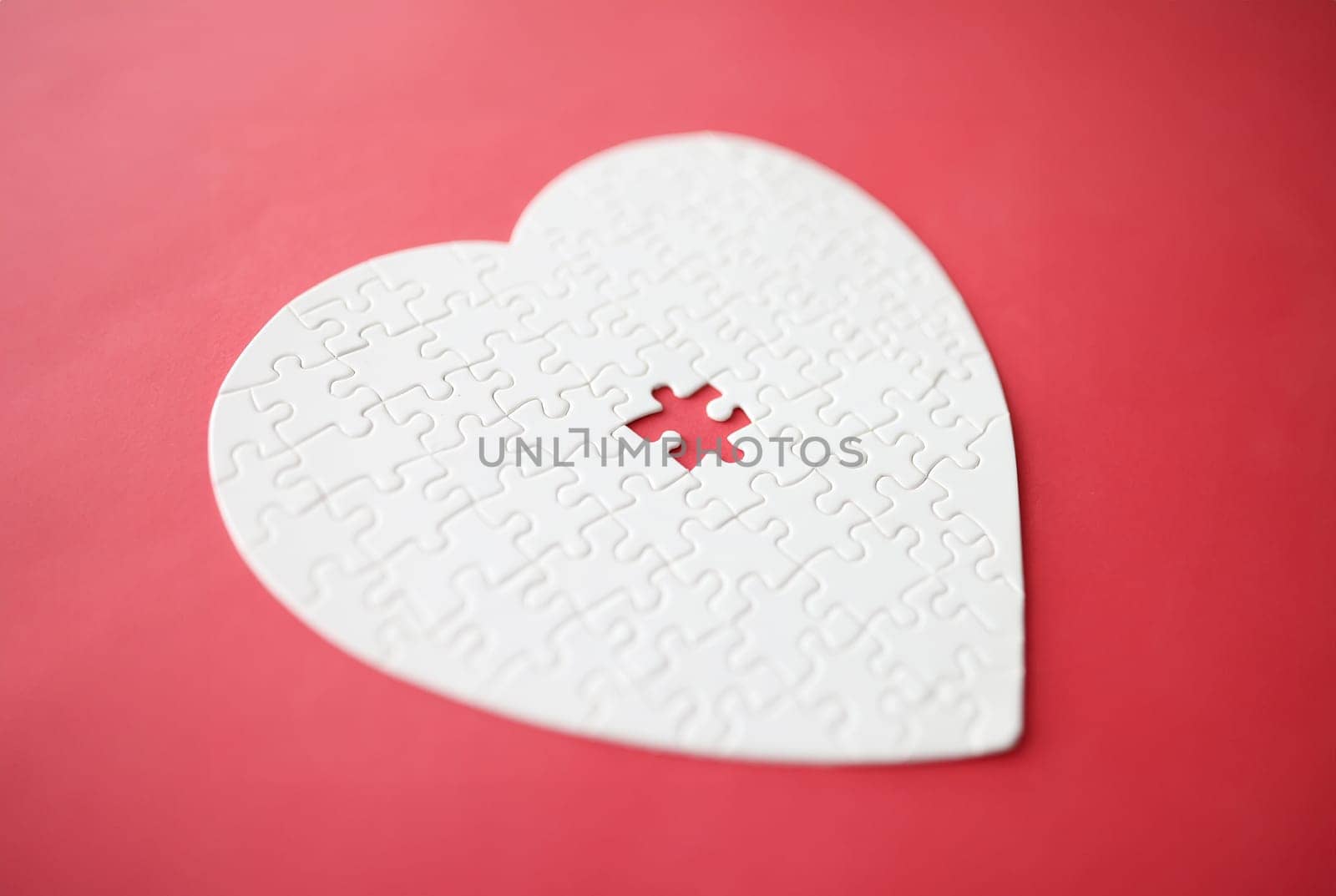 White heart made from puzzle lying on red background. Relationship problems concept