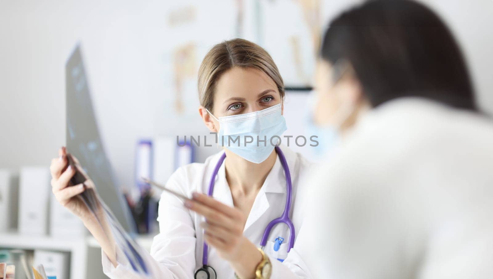 Doctor in protective mask showing patient X ray. Diagnostics of vertebral hernia concept