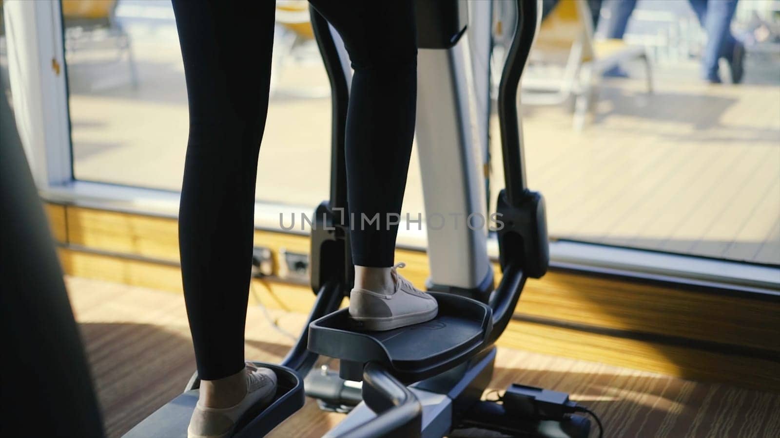 Athletic girl doing an ellipsoid in gym side view. Stock. Woman trains on an ellipsoid.
