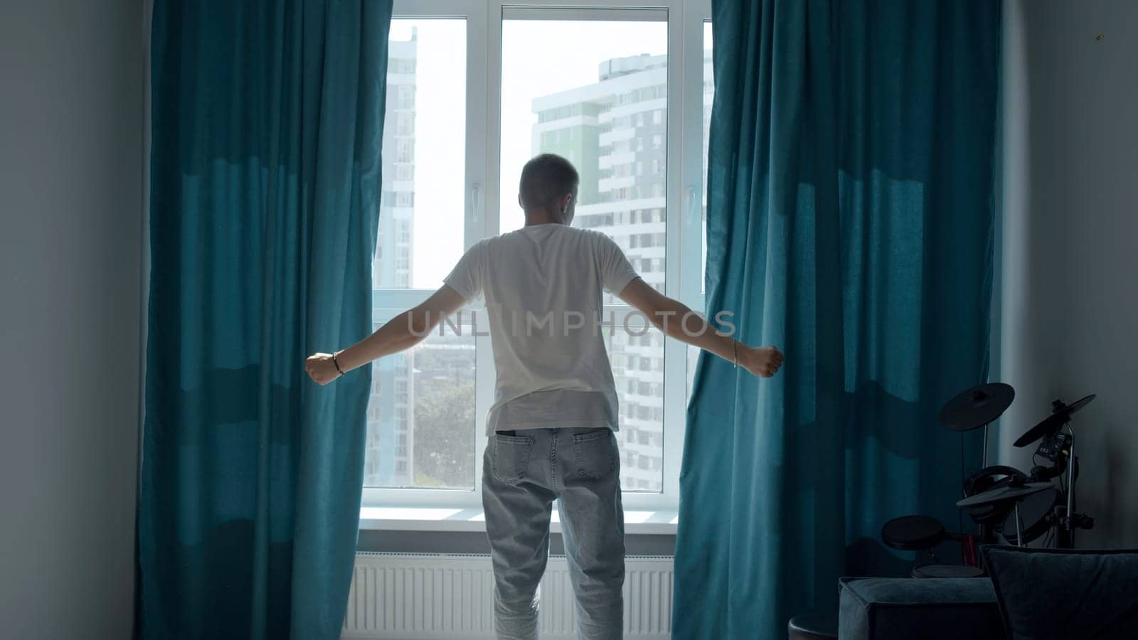 A man in a dark apartment with curtains. Media. An adult in summer clothes is a man who goes to open turquoise curtains. High quality 4k footage