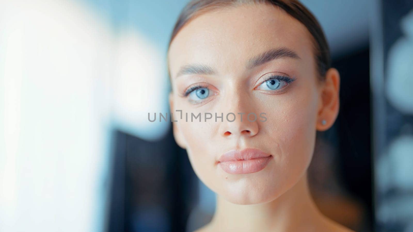 Beautiful face of tender attractive brunette woman with blue eyes staying indoors on dark blurred background. Action. Close up of confident young lady posing in front of a camera