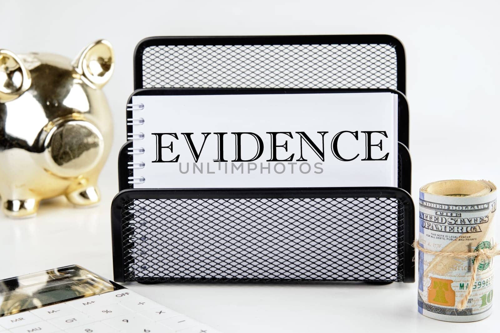 EVIDENCE text on a white piece of paper next to a piggy bank, a roll of money and a calculator on a white background
