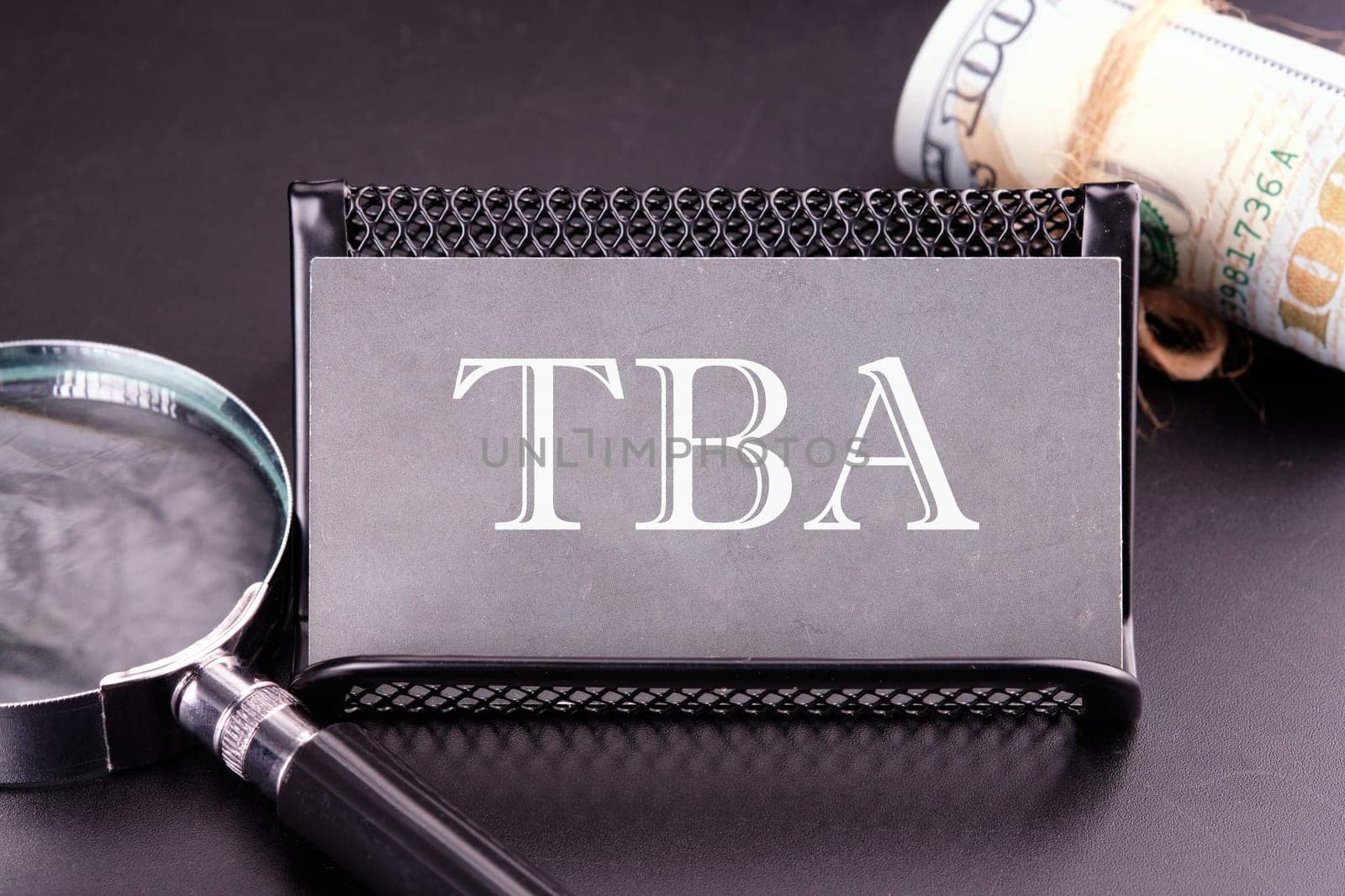 TBA text on the business card next to the money, a magnifying glass on a black background