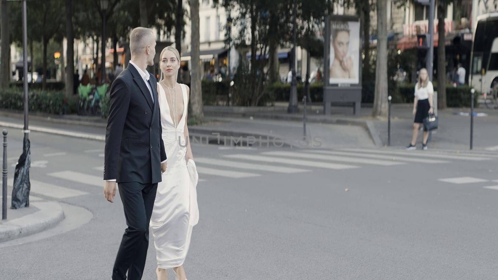 A walking European couple on a summer street. Action. Newlyweds in suits walking on the roads in hot weather. by Mediawhalestock