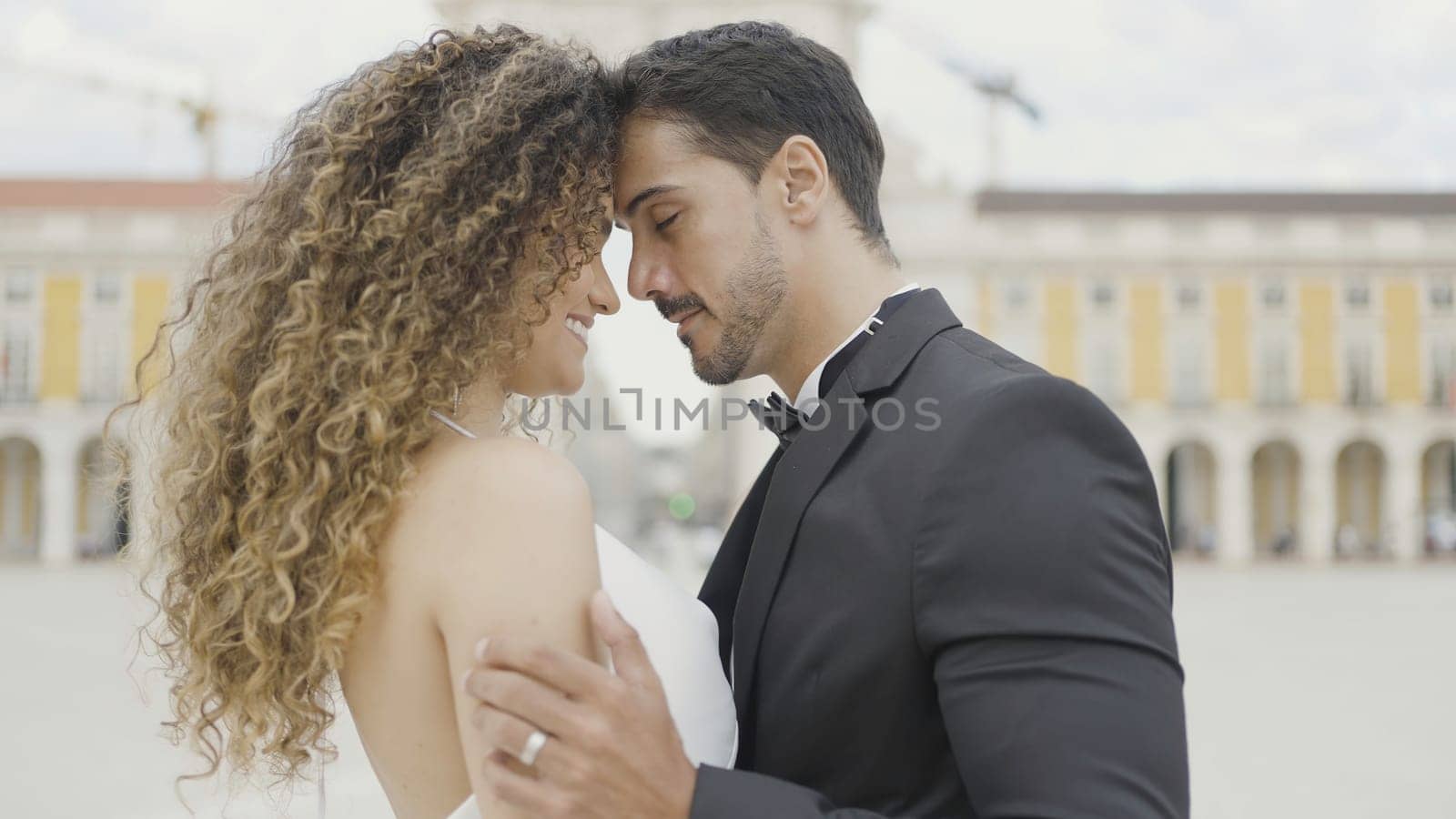Beautiful couple of lovers tenderly embrace on street. Action. Elegant couple in beautiful outfits are gently embracing. Couple in love in beautiful outfits hugs on city square by Mediawhalestock