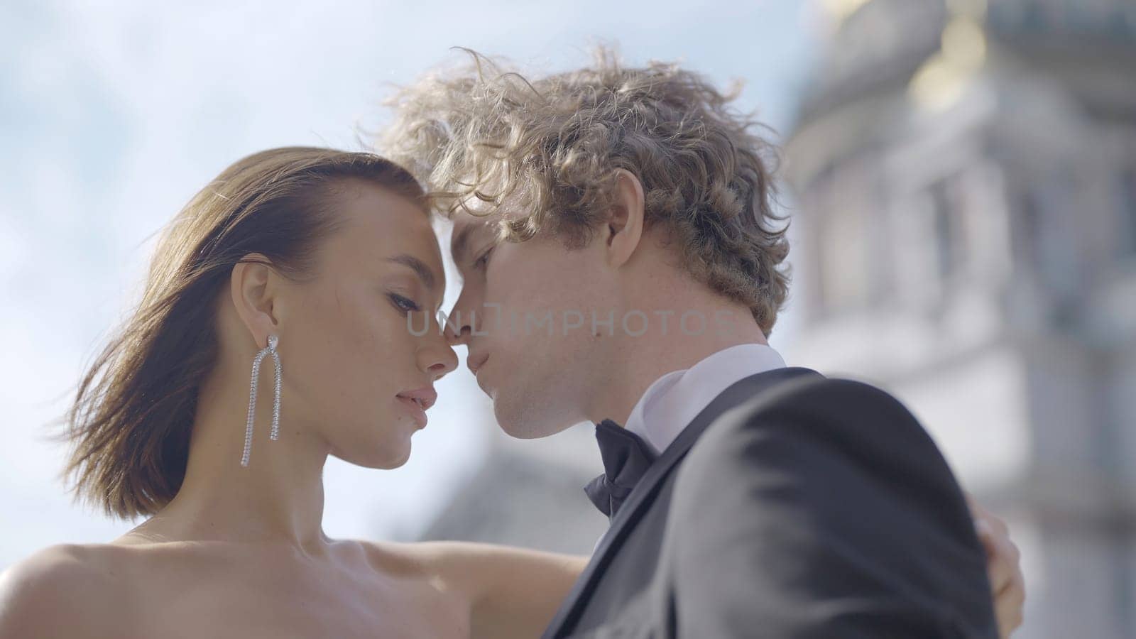 Elegant newlyweds are close to each other. Action. Passionate and stylish newlyweds on background of blue sky. Close-up of passionate tension between hugging couple.