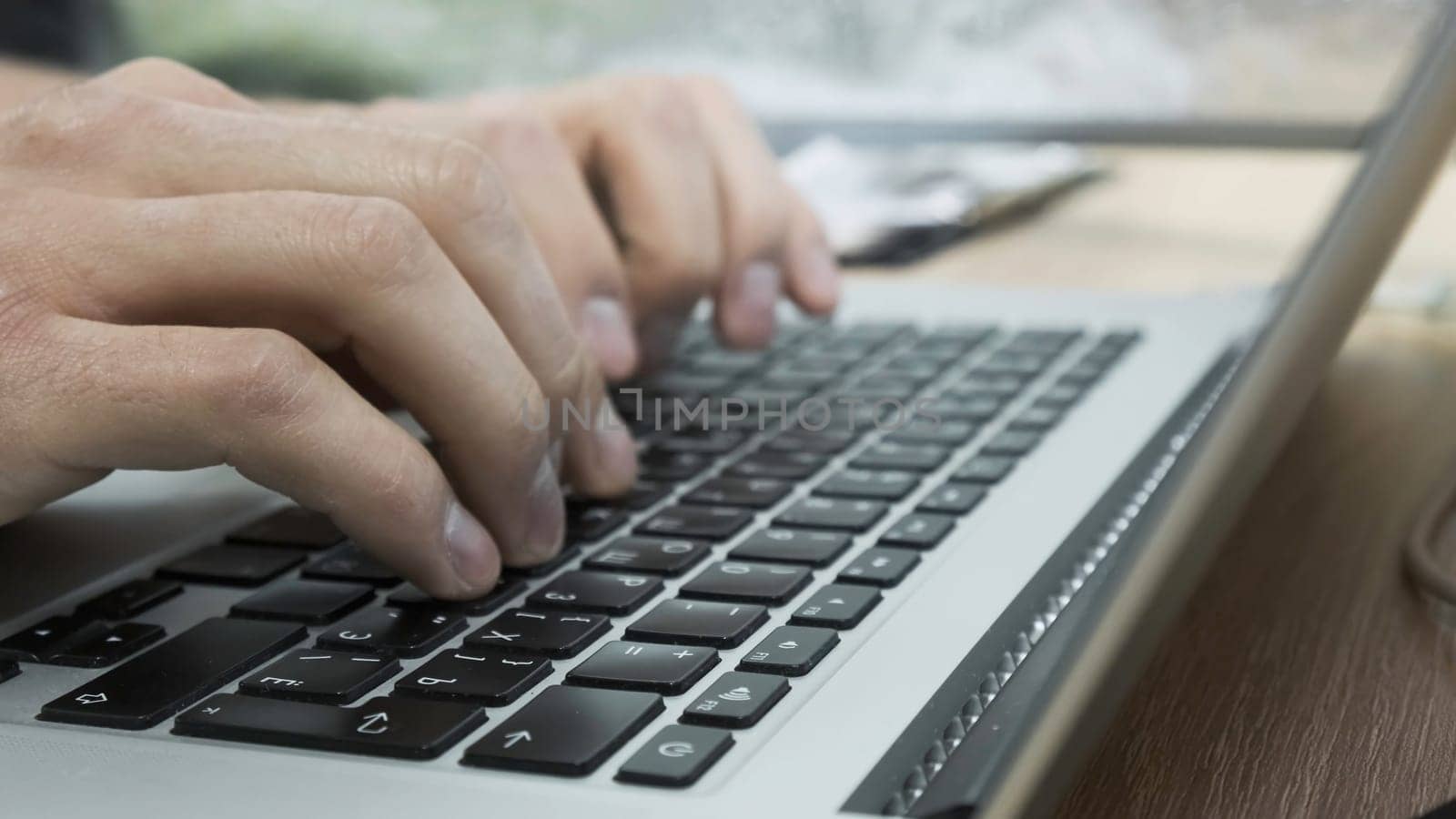 Close-up of man typing on laptop keyboard. Stock footage. Freelancer or businessman works on laptop. Men's hands print text or article on laptop.