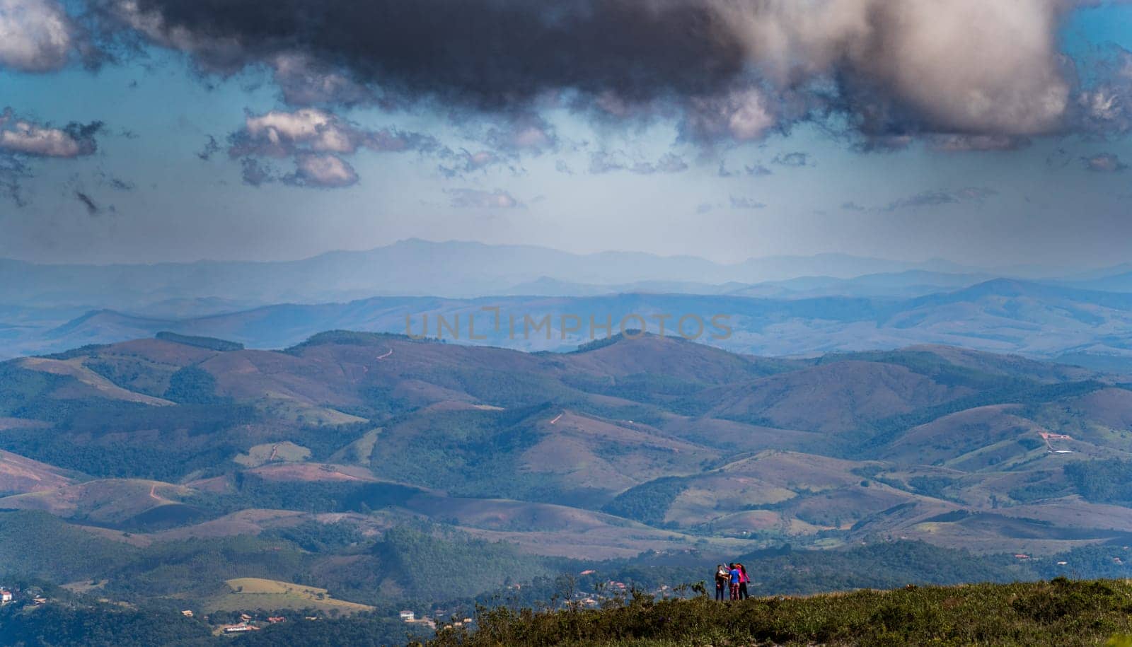 A group of hikers stand at the top of a mountain peak, enjoying the stunning view of the surrounding landscape. There is plenty of space for text.