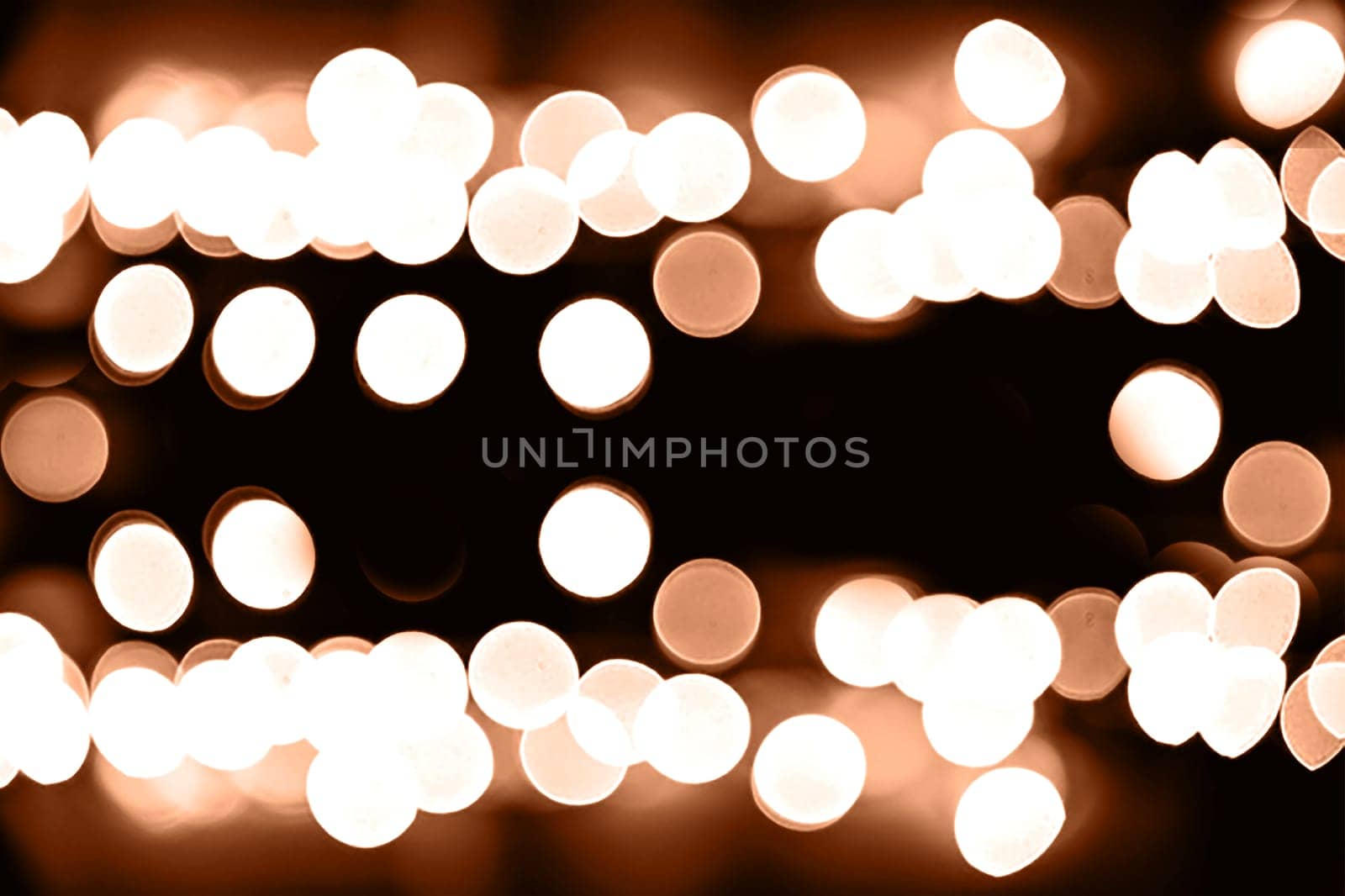 Blurry garland lights on a dark background. Festive Christmas and New Year background. Soft focus. Image toned in color of the year 2024 - Peach Fuzz.