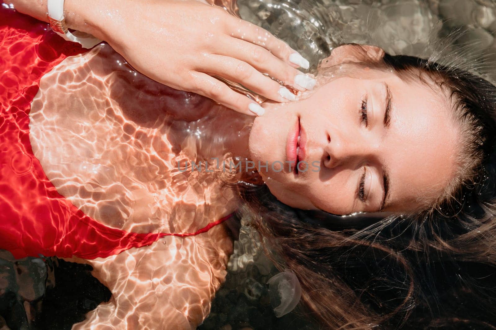 Woman travel portrait. close-up portrait of a happy woman with long hair in a red bikini, floating in water and smiling at the camera. by panophotograph