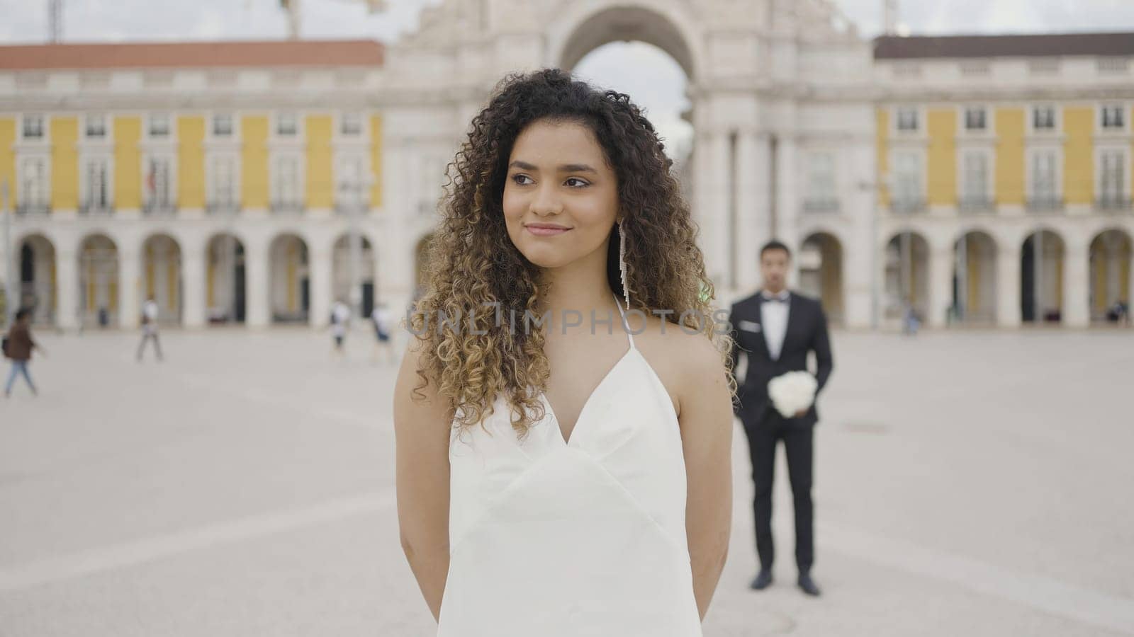 Beautiful woman in dress on background of man with bouquet of flowers. Action. Attractive woman in dress is waiting for date. Surprise man with flowers behind back of beautiful woman.