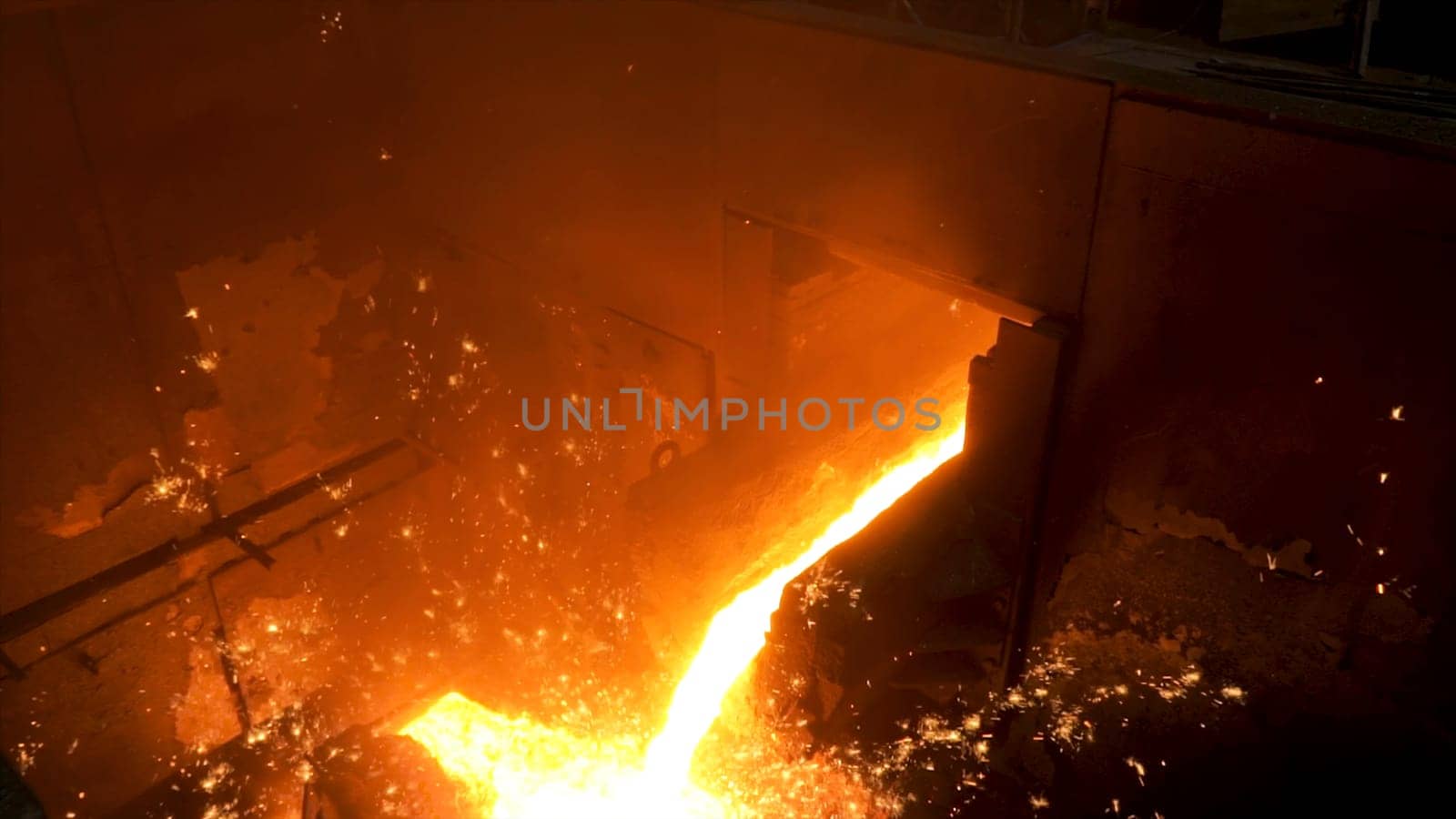 Close up for molten metal poured from ladle for casting at the foundry. Smelting of metal casting, metallurgical production at the hot shop of a factory.