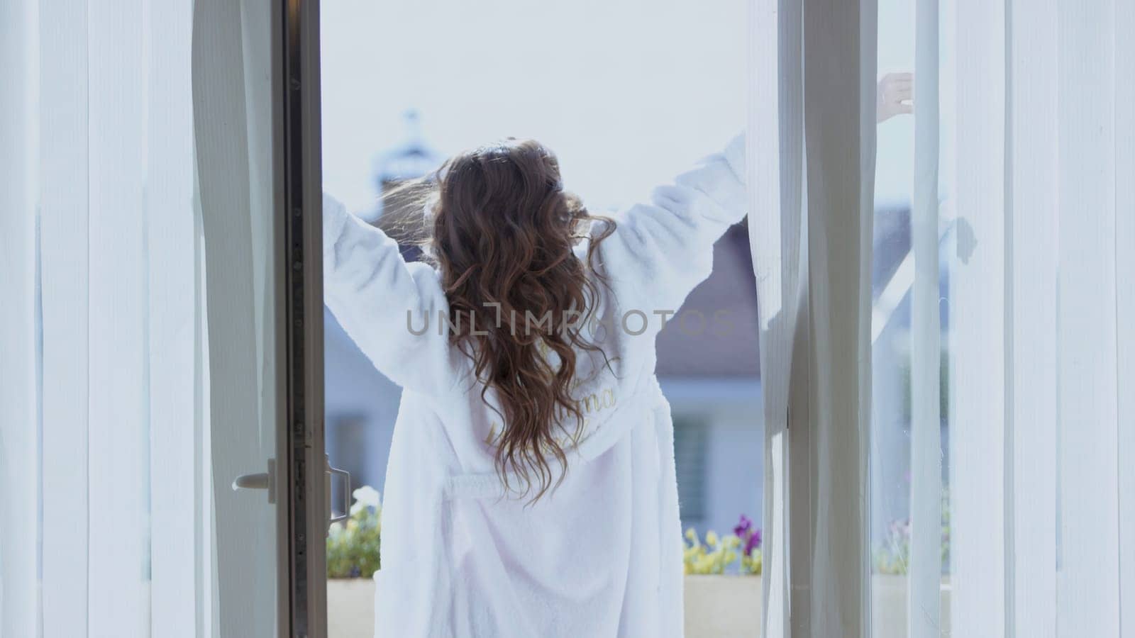 Attractive woman stretch on balcony. Video. Back view of beautiful woman in white coat stretching on balcony on sunny morning. Attractive woman on vacation abroad.