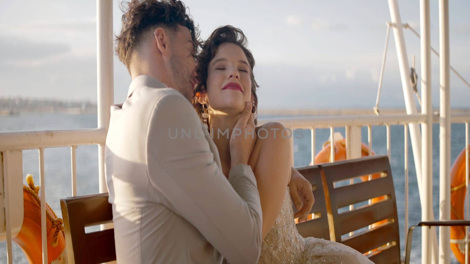 Newlyweds hug on background of cloudy sky. Action. Beautiful newlyweds happily cuddle in cloudy weather. Happy newlyweds in stylish outfits hug in windy weather.