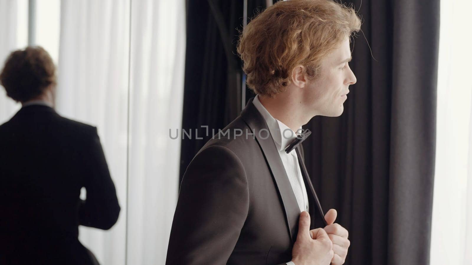 A man with a sympathetic appearance . Action . A man in an elegant suit stands next to the mirror and poses