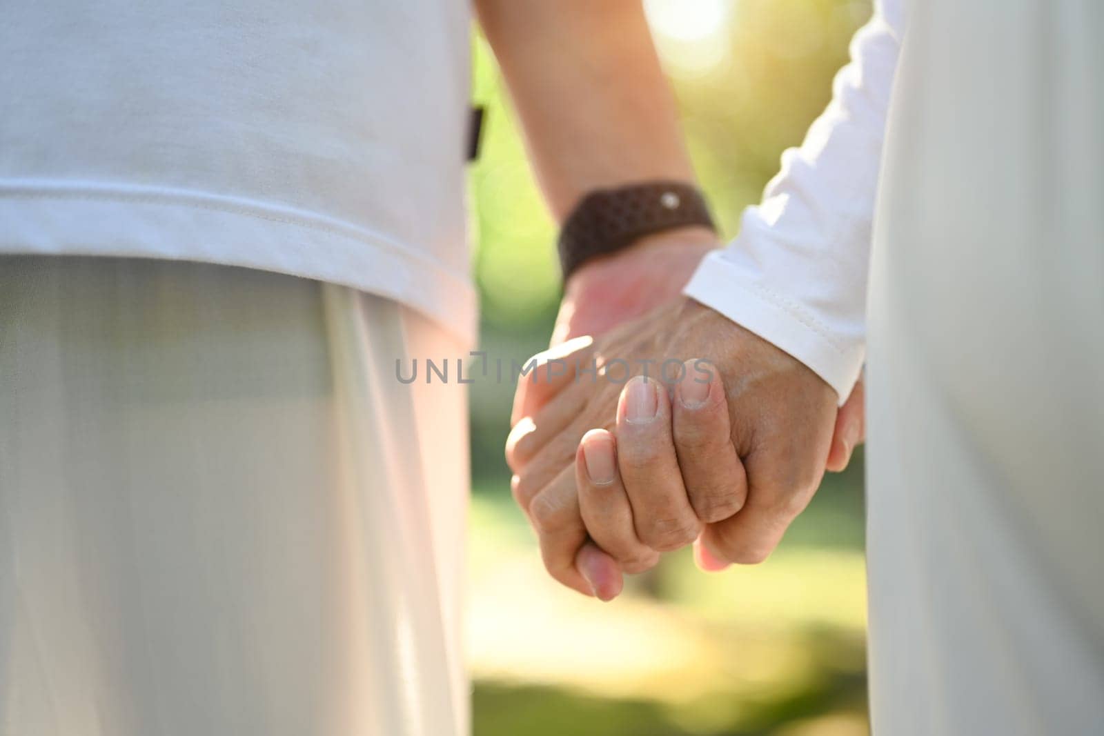 Close up of elderly couple holding hands while walking in the nature during sunrise. by prathanchorruangsak