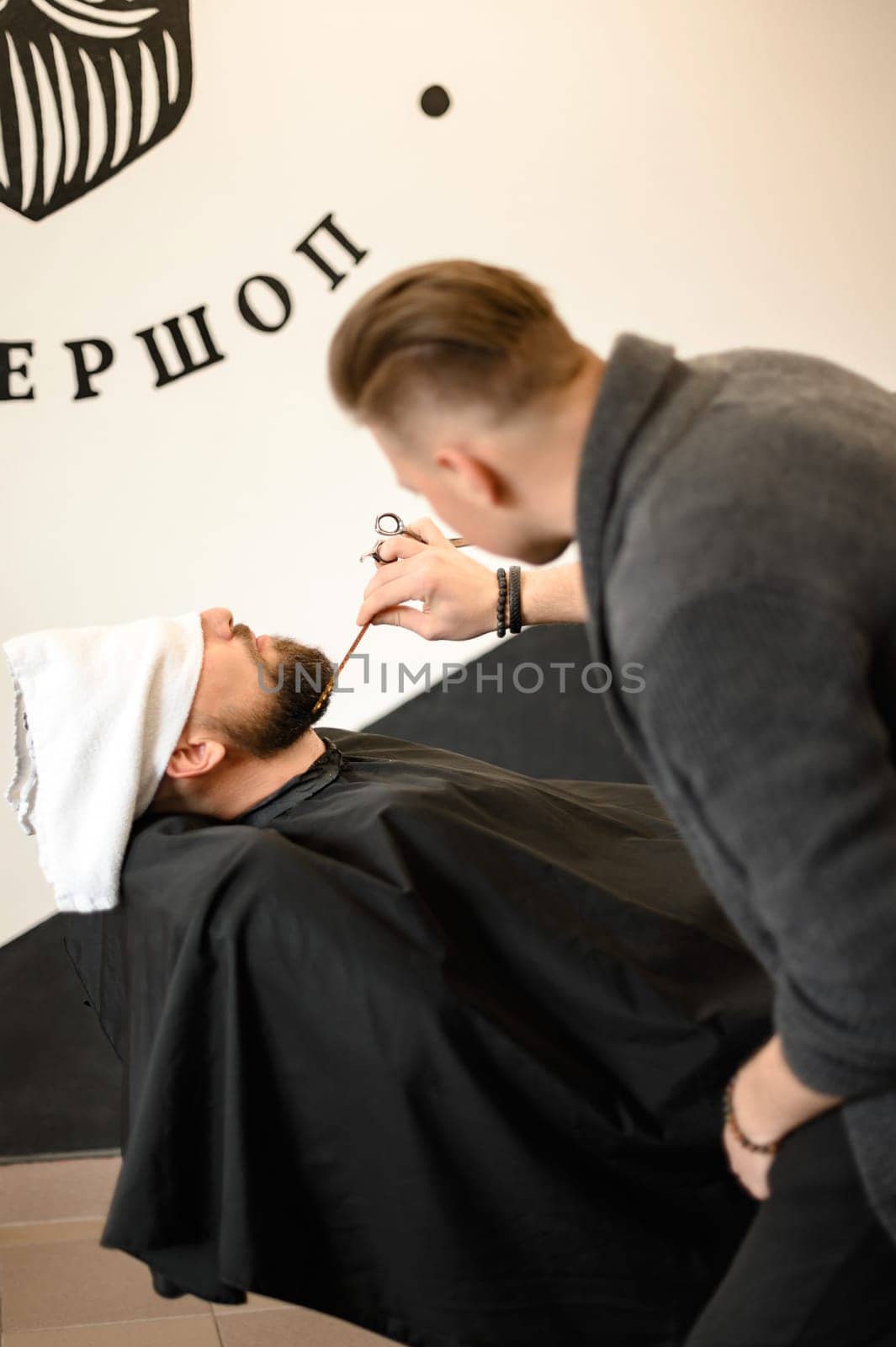 Barber combs beard with comb while shaving Caucasian man by Niko_Cingaryuk