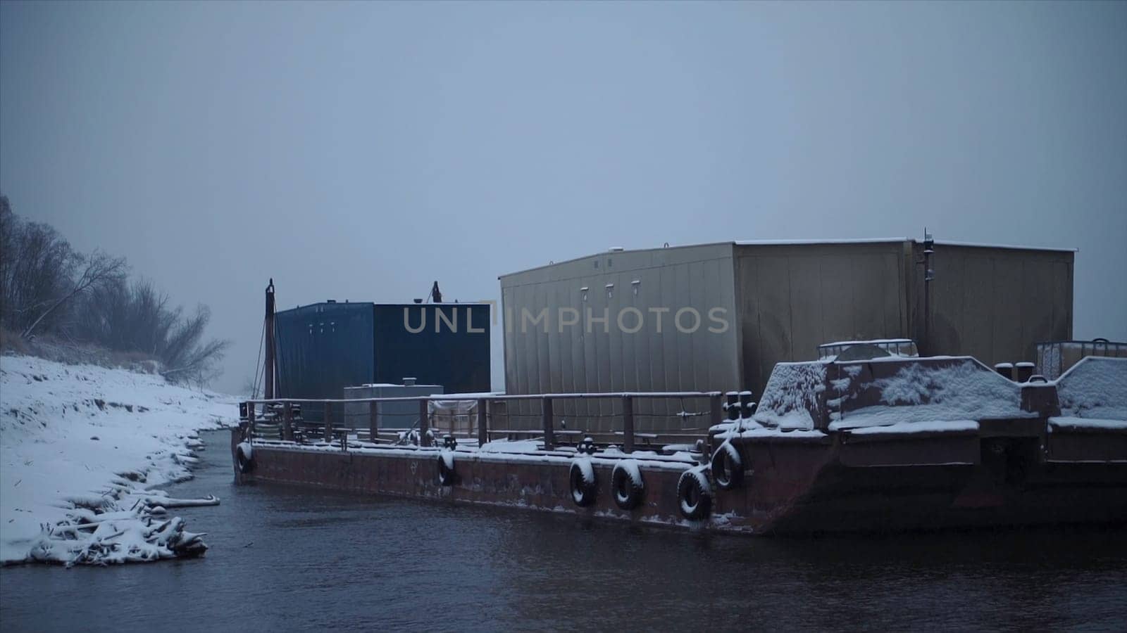 Barge with containers on river in winter. Clip. Barge transports cargo with containers along river in winter. Winter river transportation by barge.