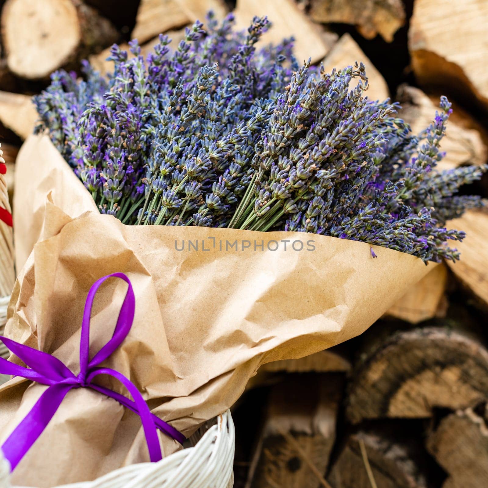 A lush and large bouquet of lavender wrapped in brown paper on a background of firewood
