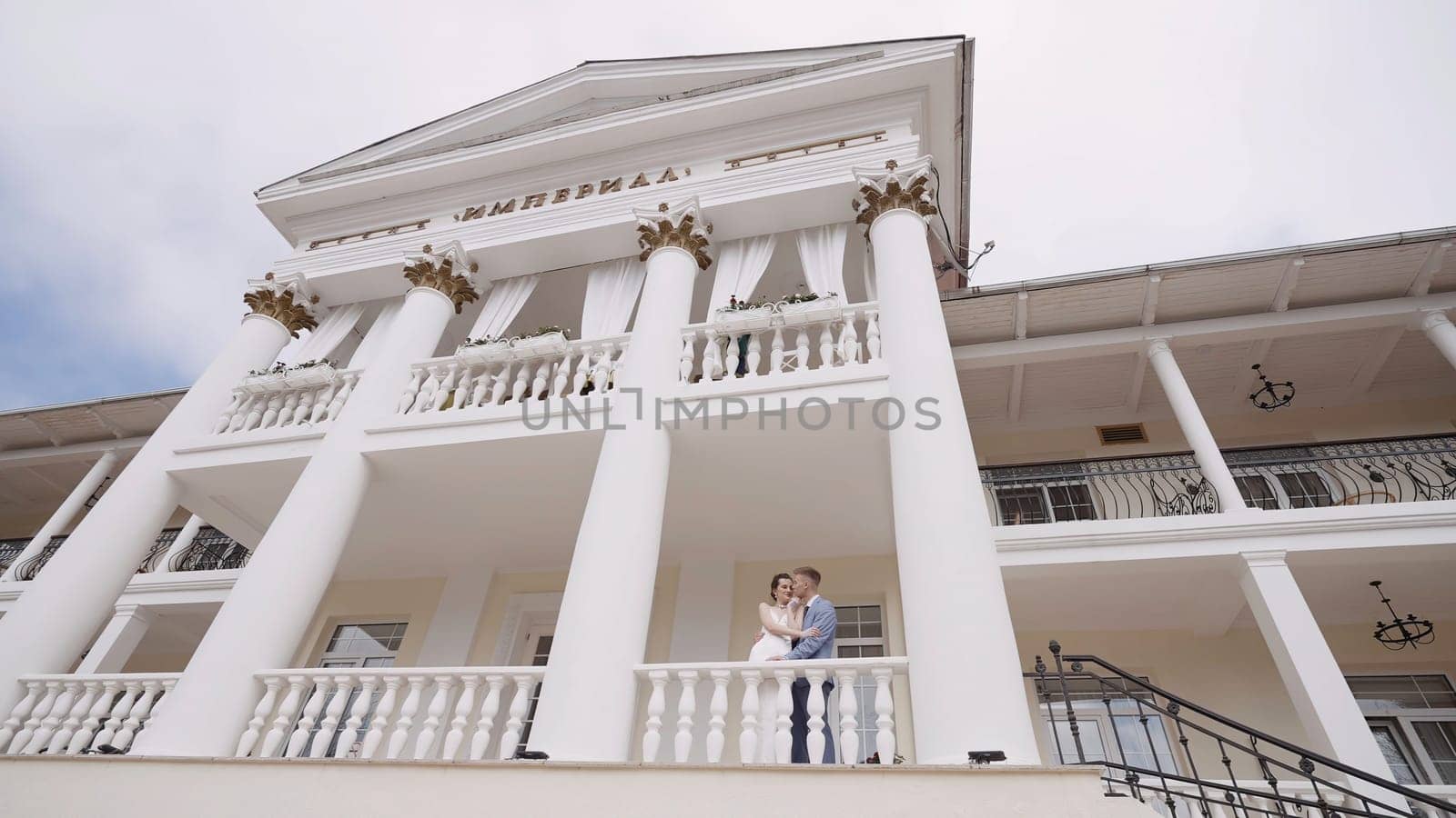 Newlyweds kiss in building with columns. Action. View below is of beautiful white building with columns and newlyweds. Newlyweds in beautiful white building.