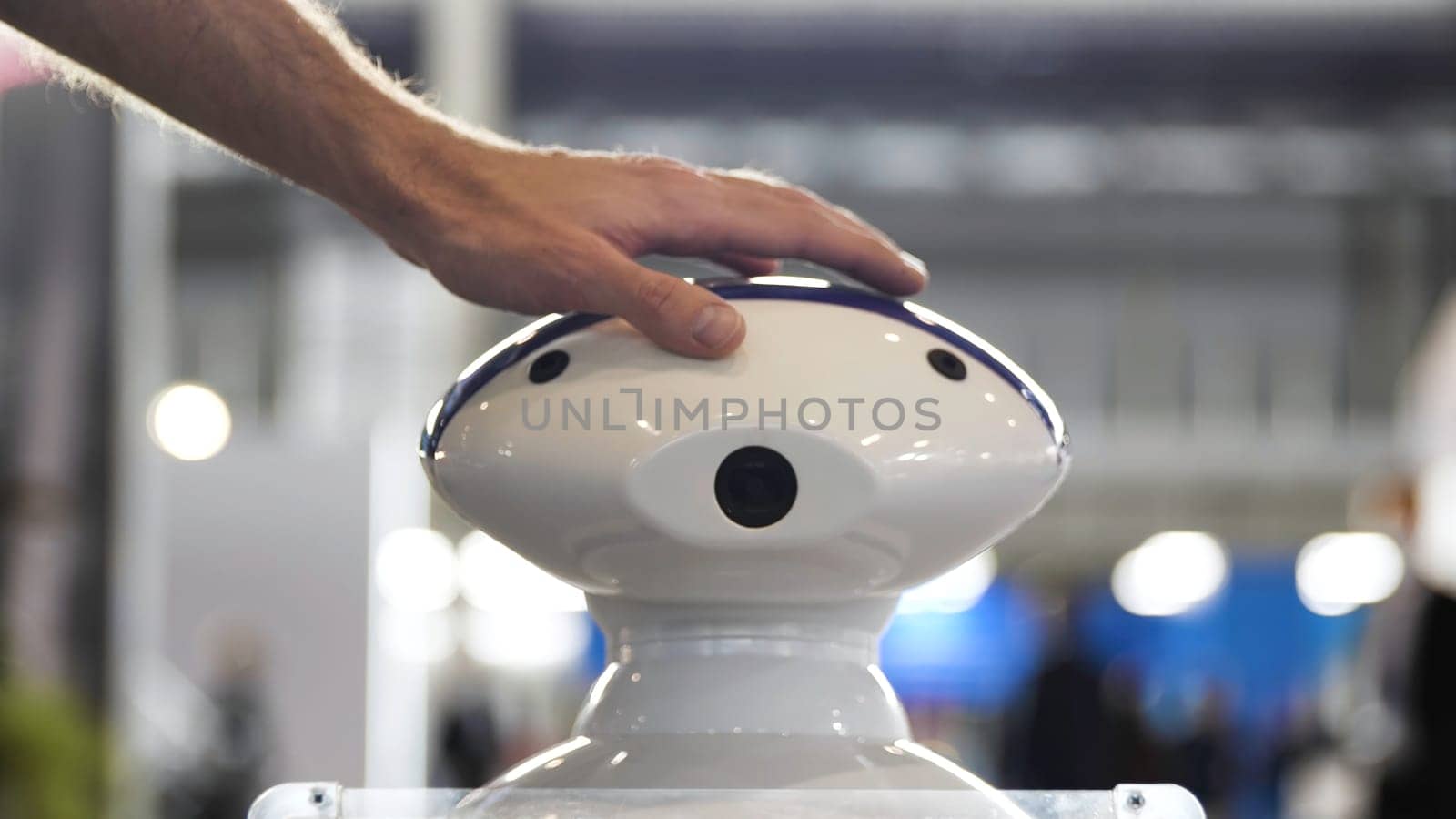 Close up of male hand touching a head of a robot at the exhibition. Man patting on the head of a moving plastic humanoid robot, concept of modern technologies.