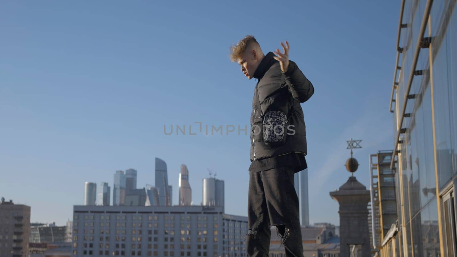 Guy is dancing cool on background of modern city. Action. Young man is dancing with view of city on sunny day. Modern dance of young man at glass building in modern city.