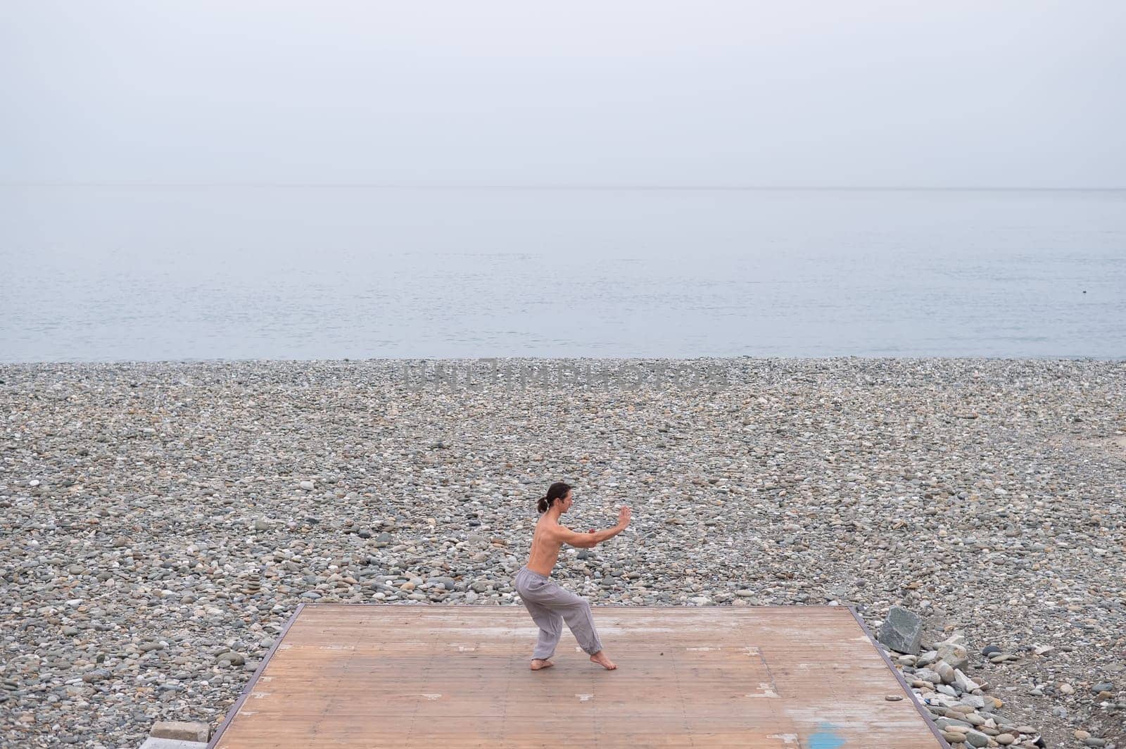 Caucasian man with naked torso practicing wushu on the seashore