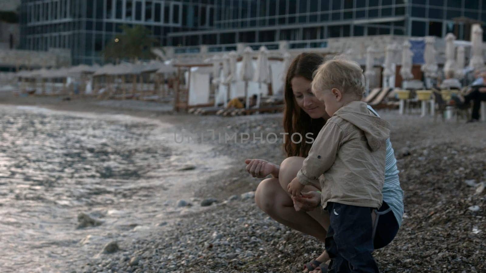 Rear view of a boy and his mother on pebble beach on a summer day. Creative. Concept of vacation. little child throwing stones