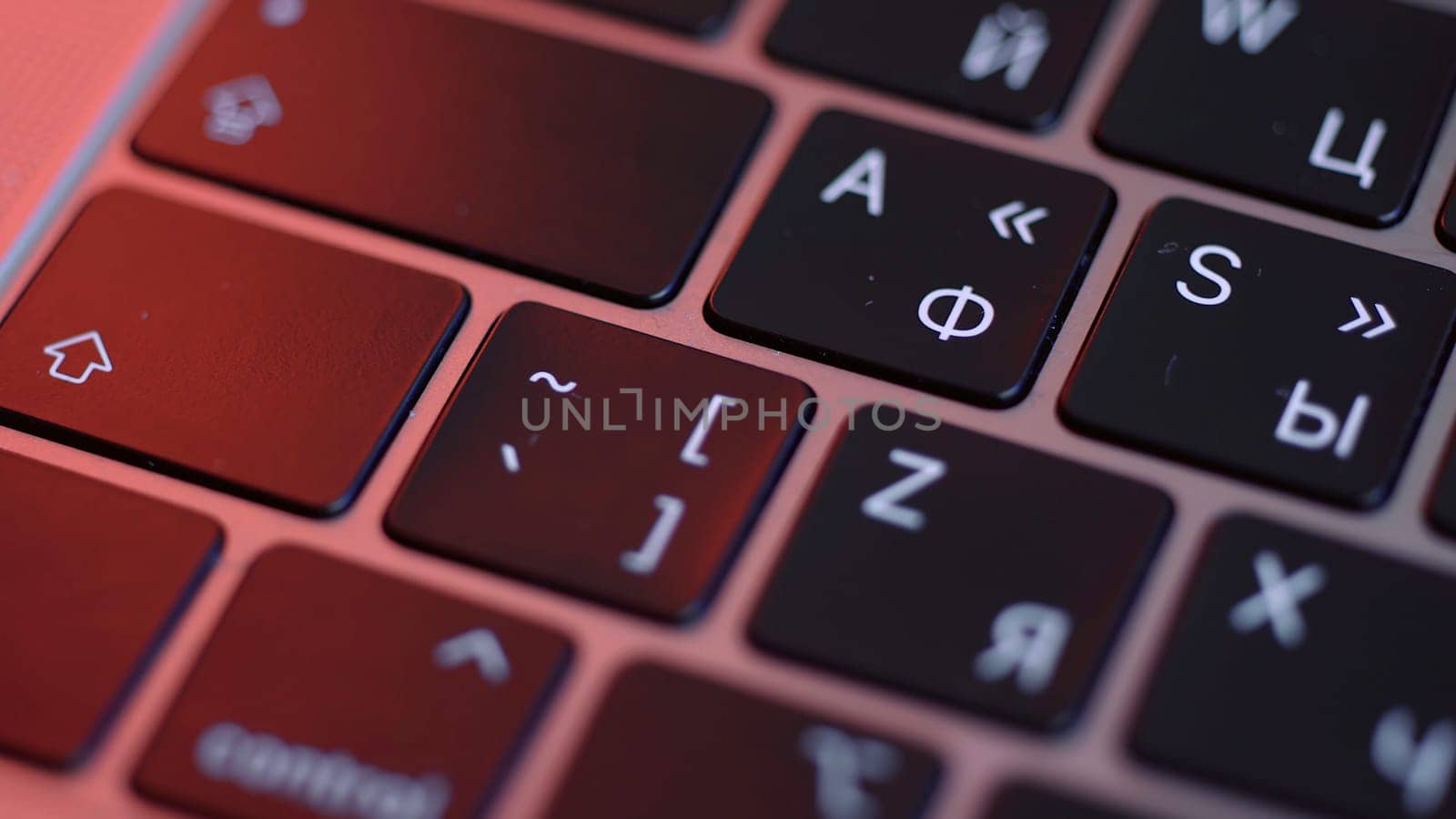 Close up of buttons on computer keyboard, macro background. Black modern laptop buttons under the red lamp light, concept of technologies and devices.