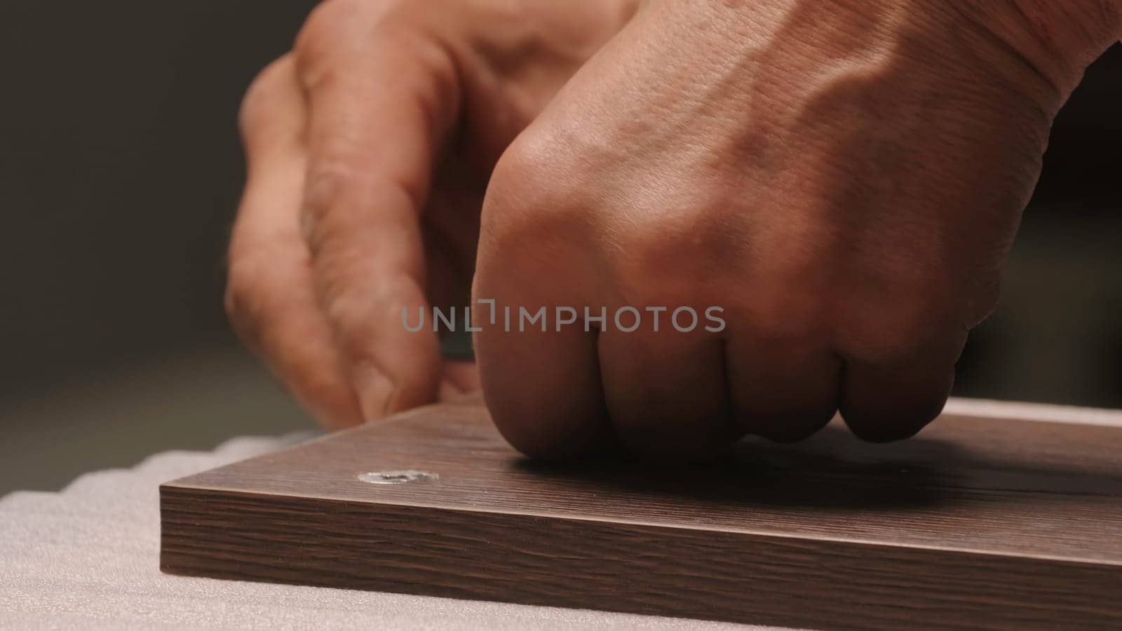 Close-up of man inserts screw into board. Creative. Man screws screw into wooden board. Worker screws screw into board and takes it away.