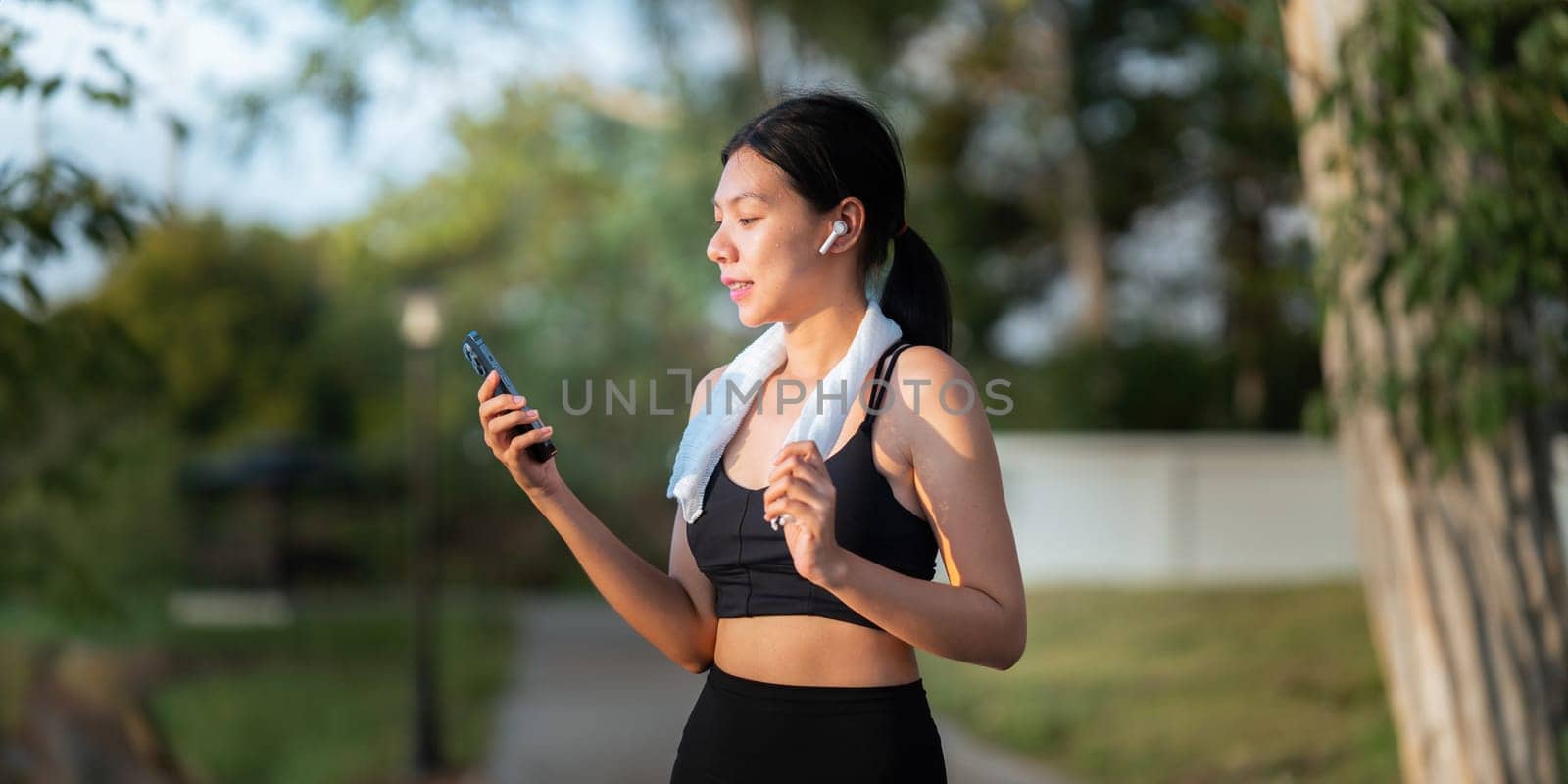 Portrait of smiling Asian woman looking at her smartphone and reading on application, standing in park wearing sport uniform.