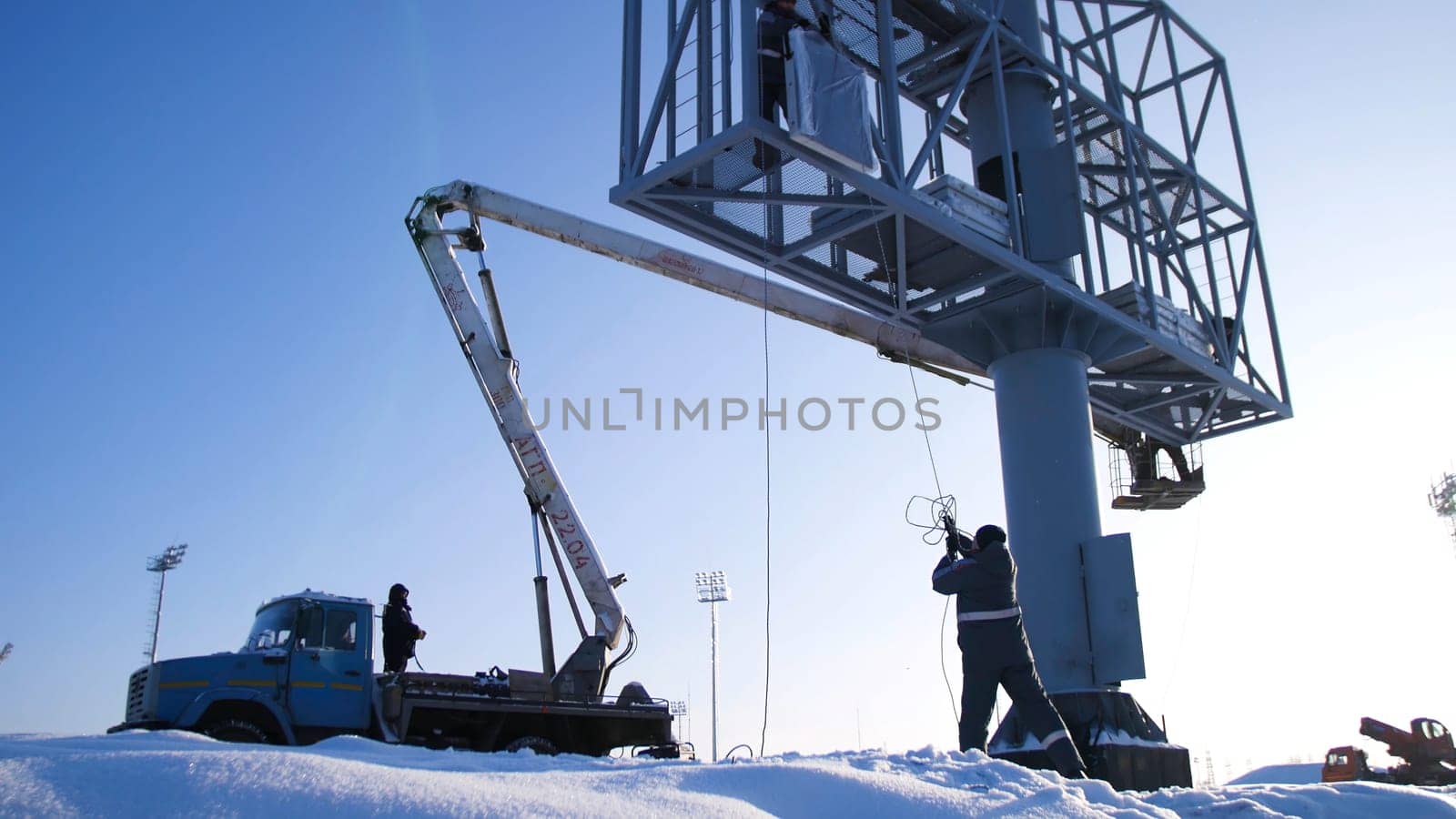 Men assemble Billboard on tap. Builder on a Lift Platform at a construction site. Man rises to the top part of the Billboard for advertising.