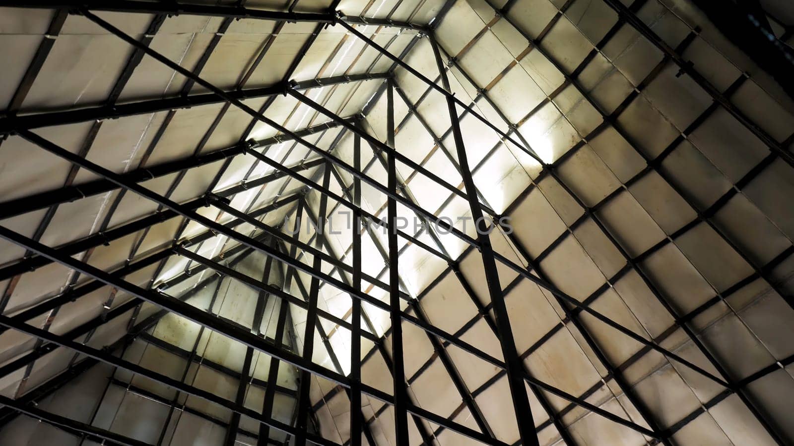 Metal sections of the roof of an industrial warehouse. Bottom view of triangular roof made of plywood sheets with steel structure of metal beams.