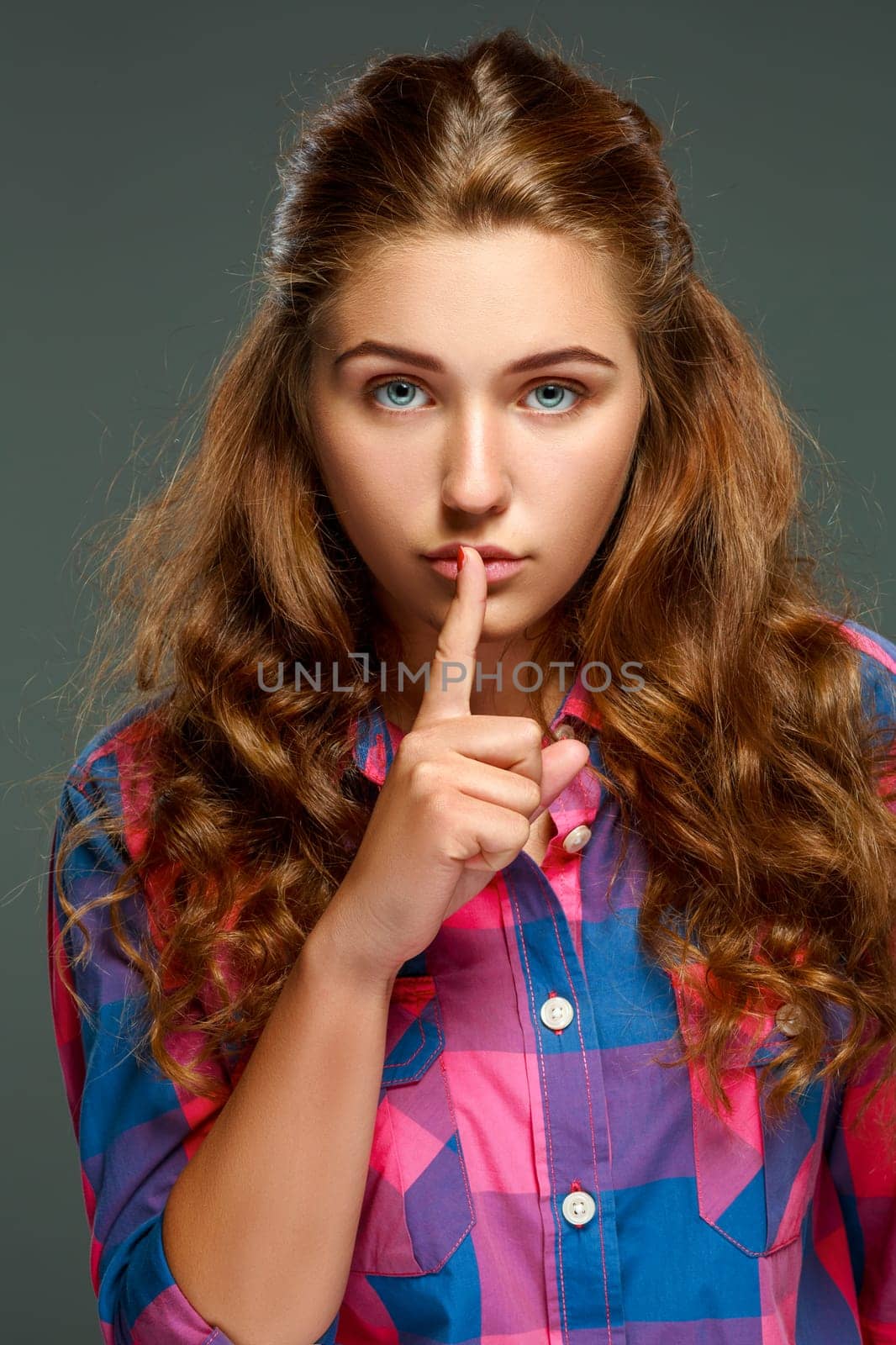 Portrait playful young brunette woman with wavy hair, looking at the camera, isolated on dark background