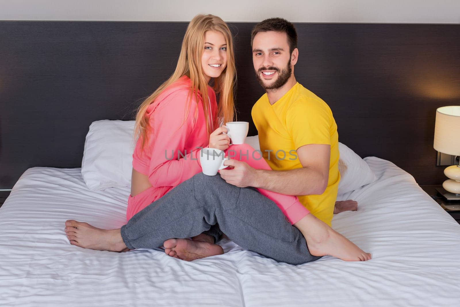 Happy young couple having breakfast tray on bed at home in bedroom. Young couple drink coffee in bed, happy smile