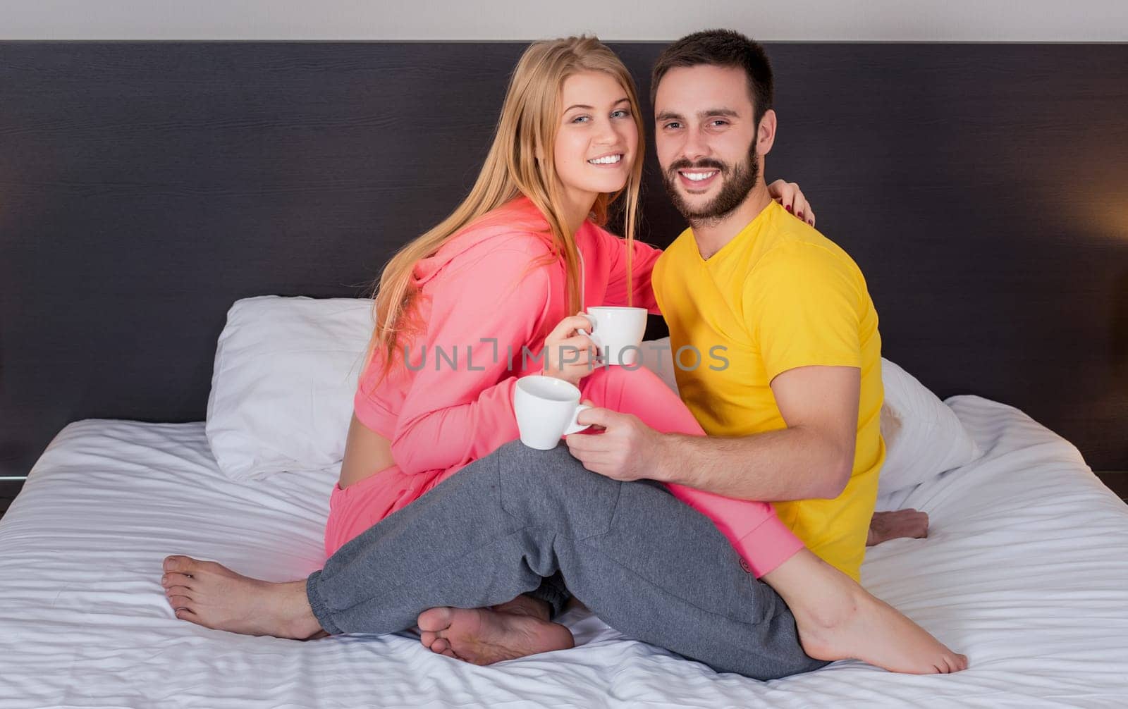 Happy young couple having breakfast tray on bed at home in bedroom. Young couple drink coffee in bed, happy smile